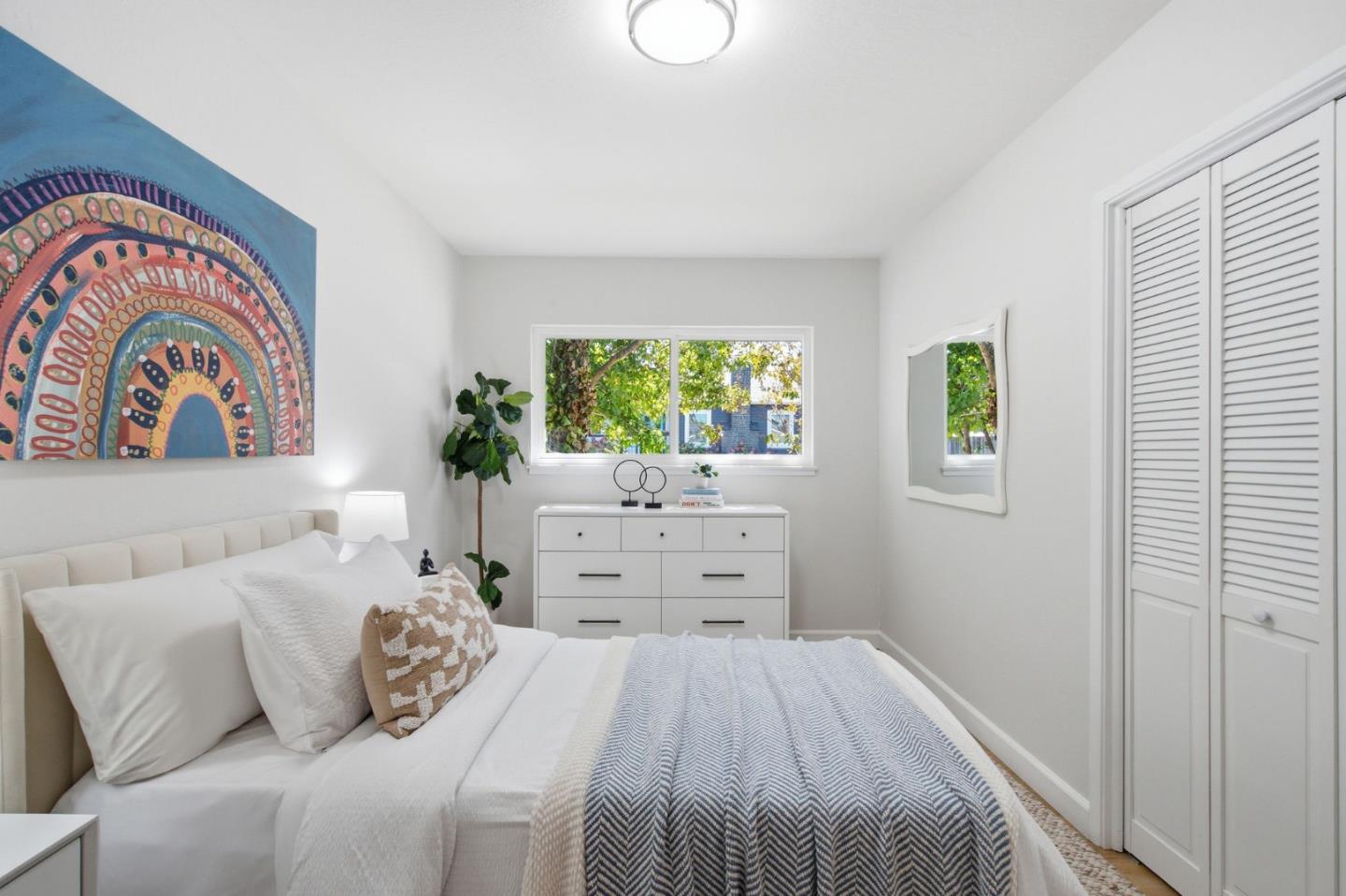 Staged bedroom with colorful circular wall art, a white bed, and louvered closet doors.