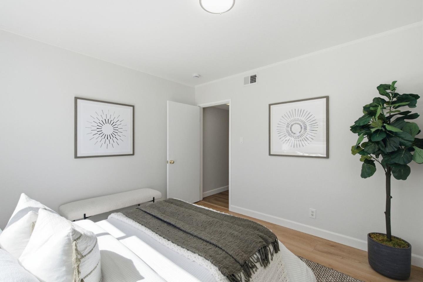 Bedroom with a white bed, gray throw, framed radial prints, and a potted plant.