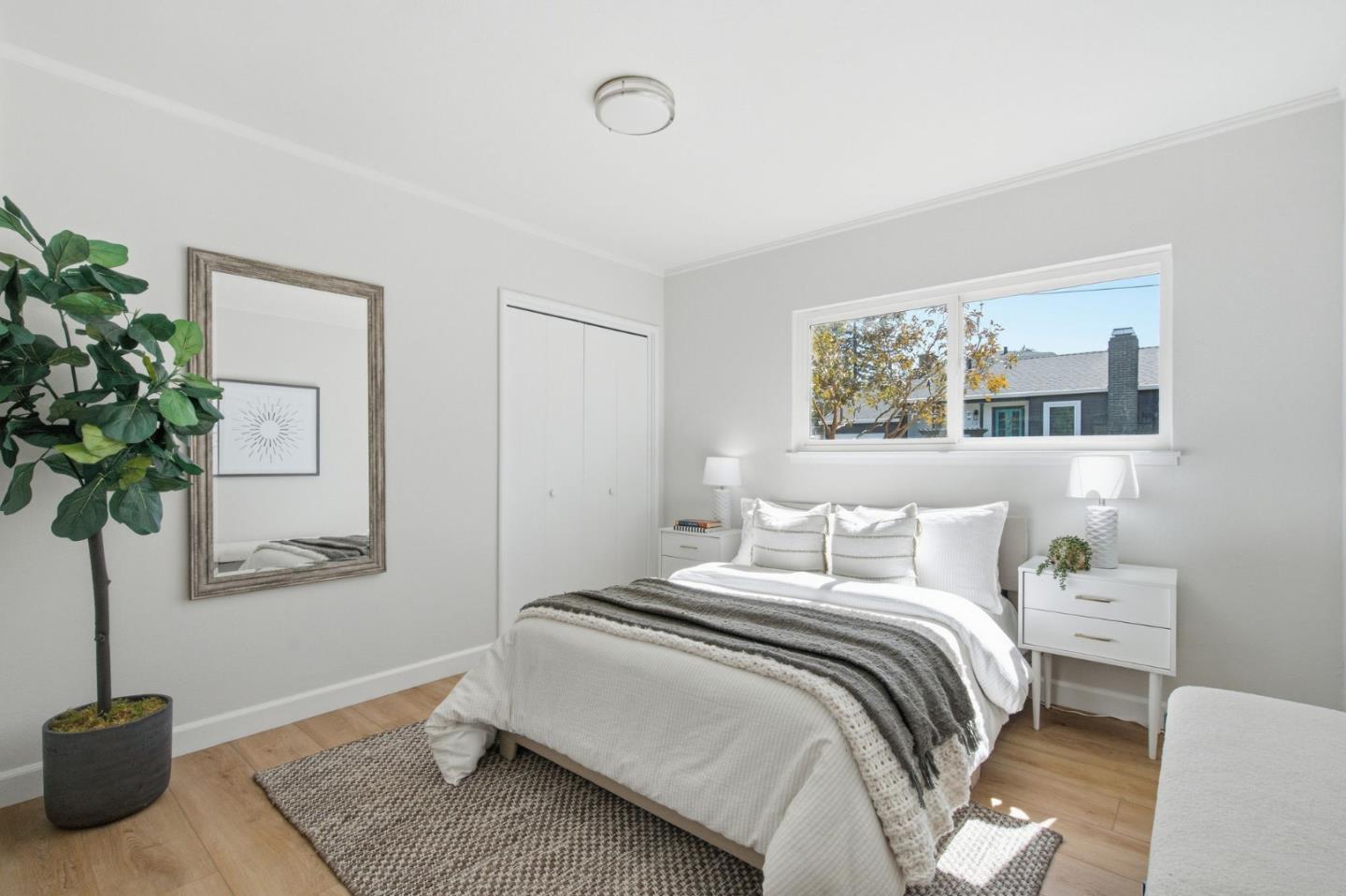 Bright bedroom with a white bed, gray throw, large window, and potted plant.