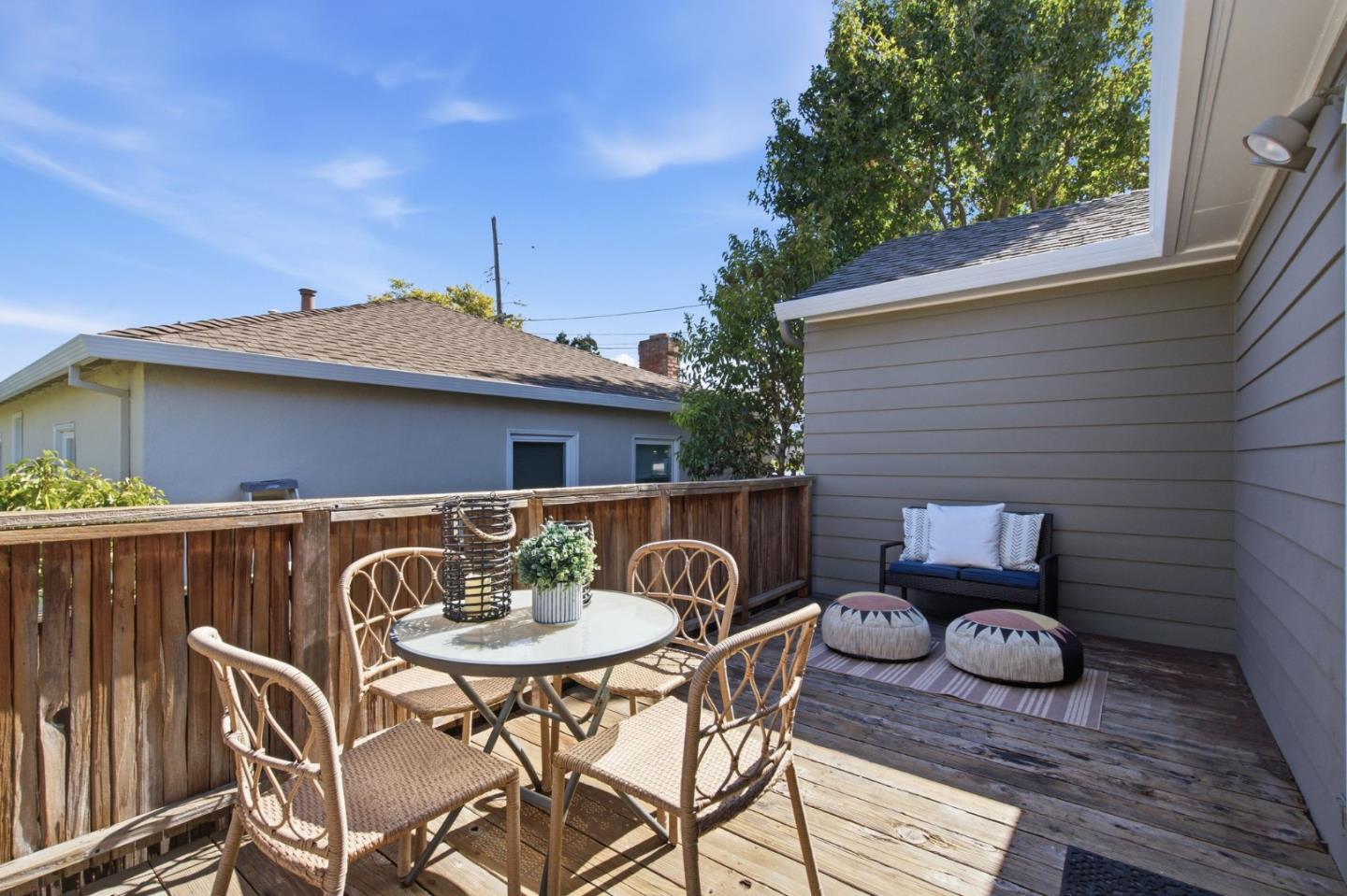 Furnished wooden deck with a round dining set and a cushioned loveseat beside the house.