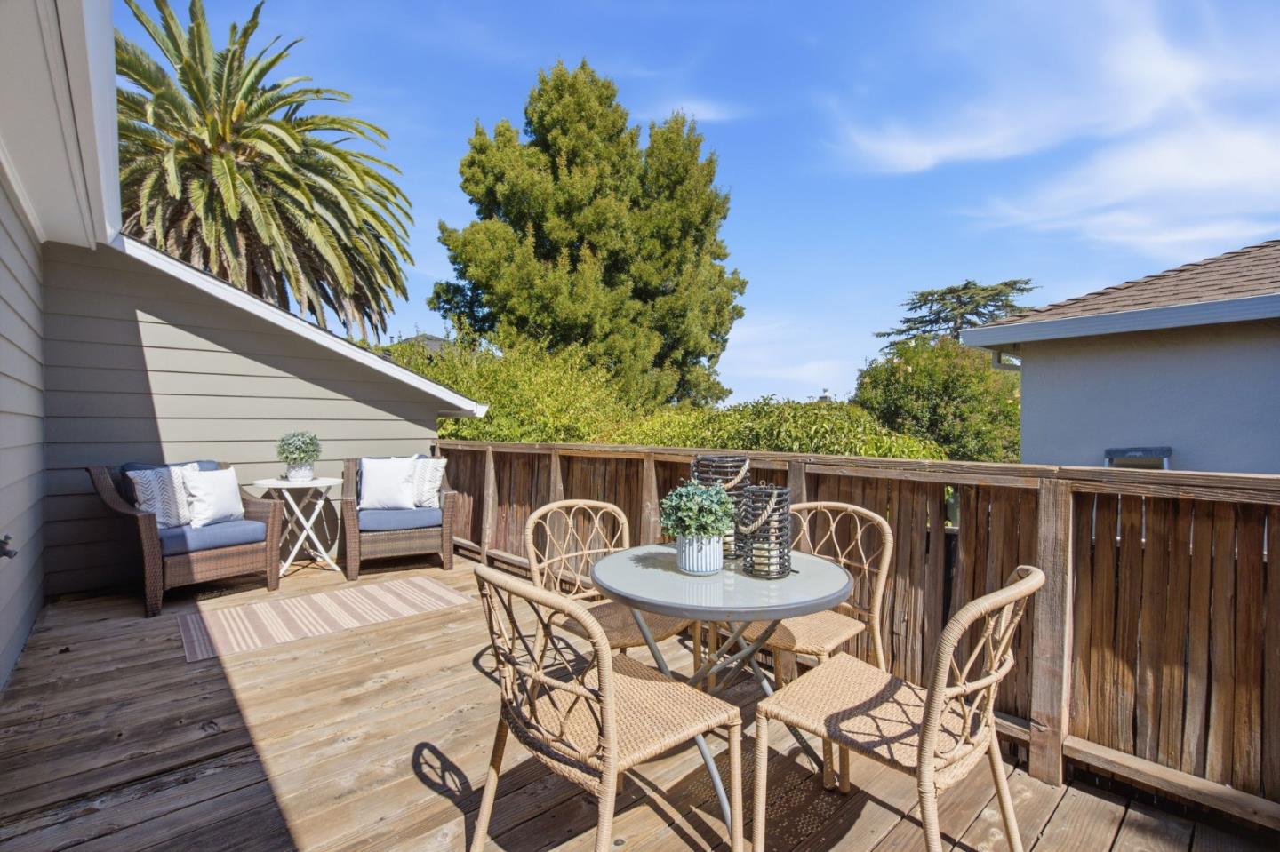 Furnished wooden deck with wicker dining set, cushioned seating, and a wooden railing.