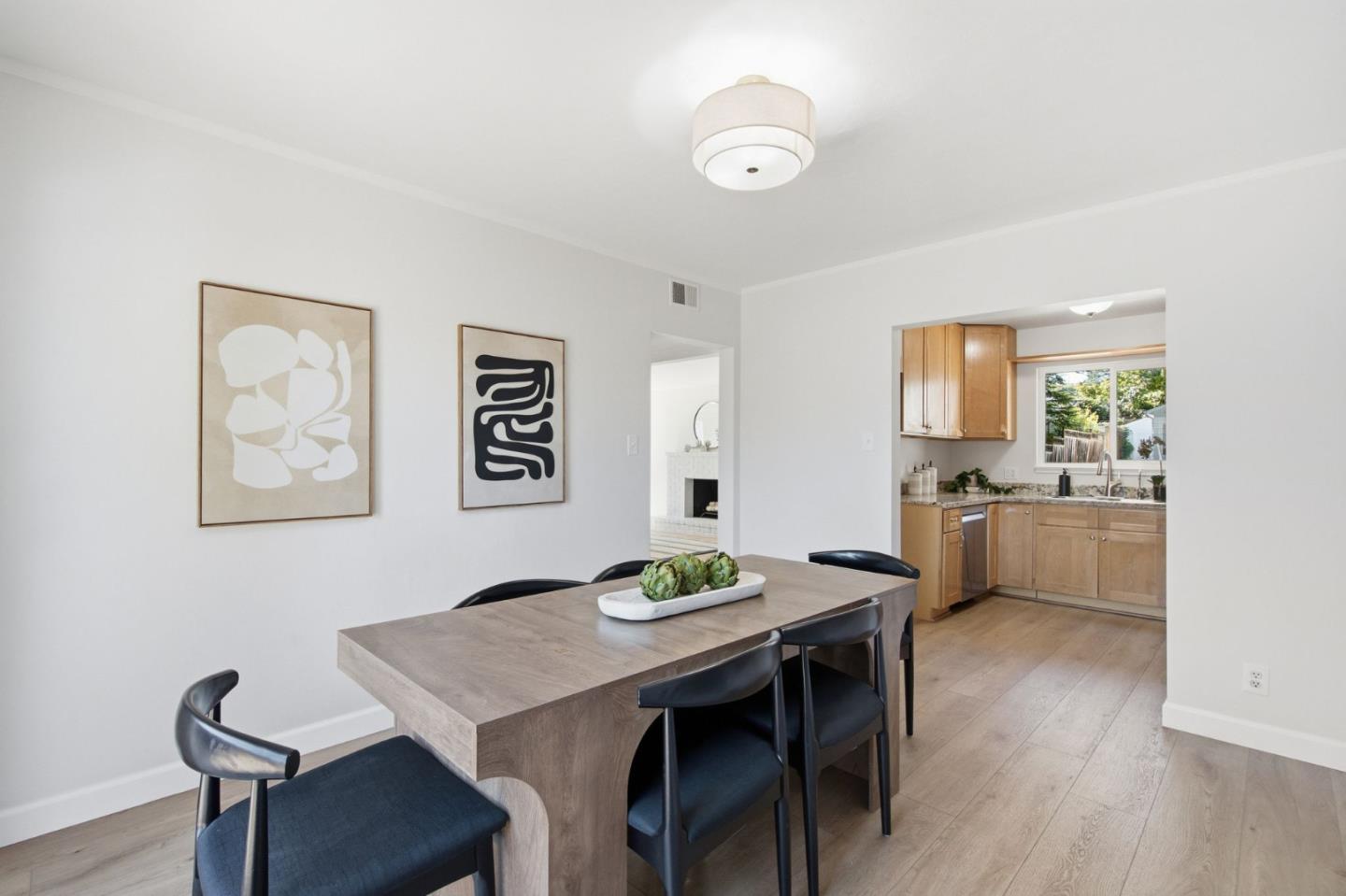 Dining room with a wood table and dark chairs beside an adjoining kitchen with wood cabinets.
