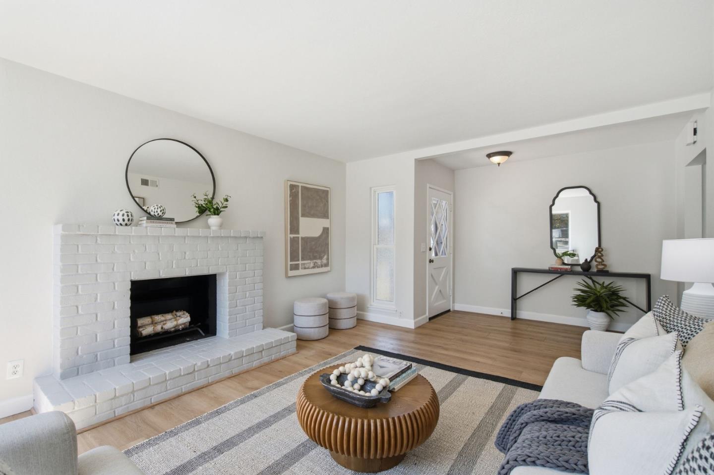 Staged living room with a white brick fireplace and round fluted wood coffee table.