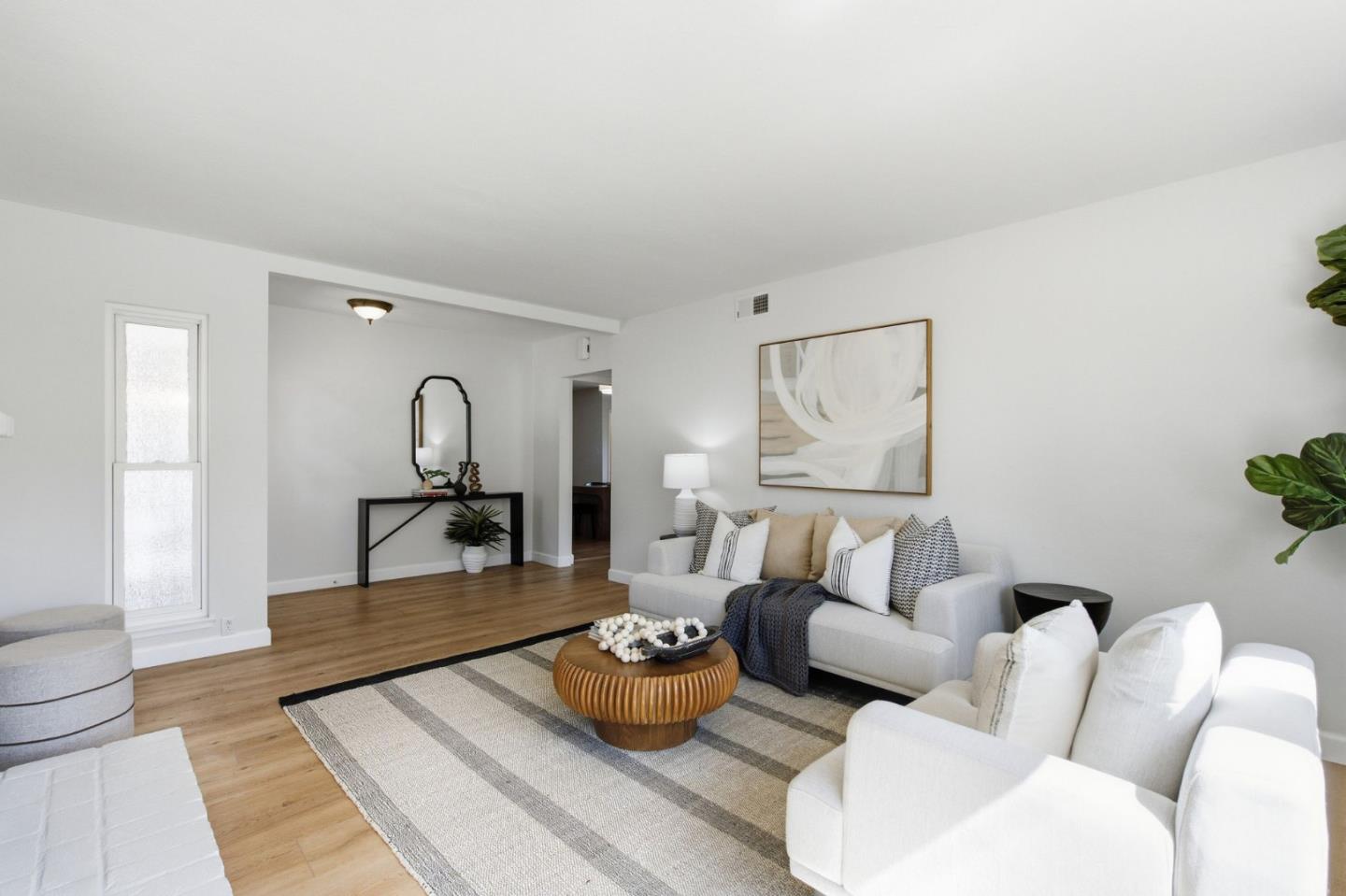 Staged living room with white sofas, a round wood coffee table, and hardwood floors.