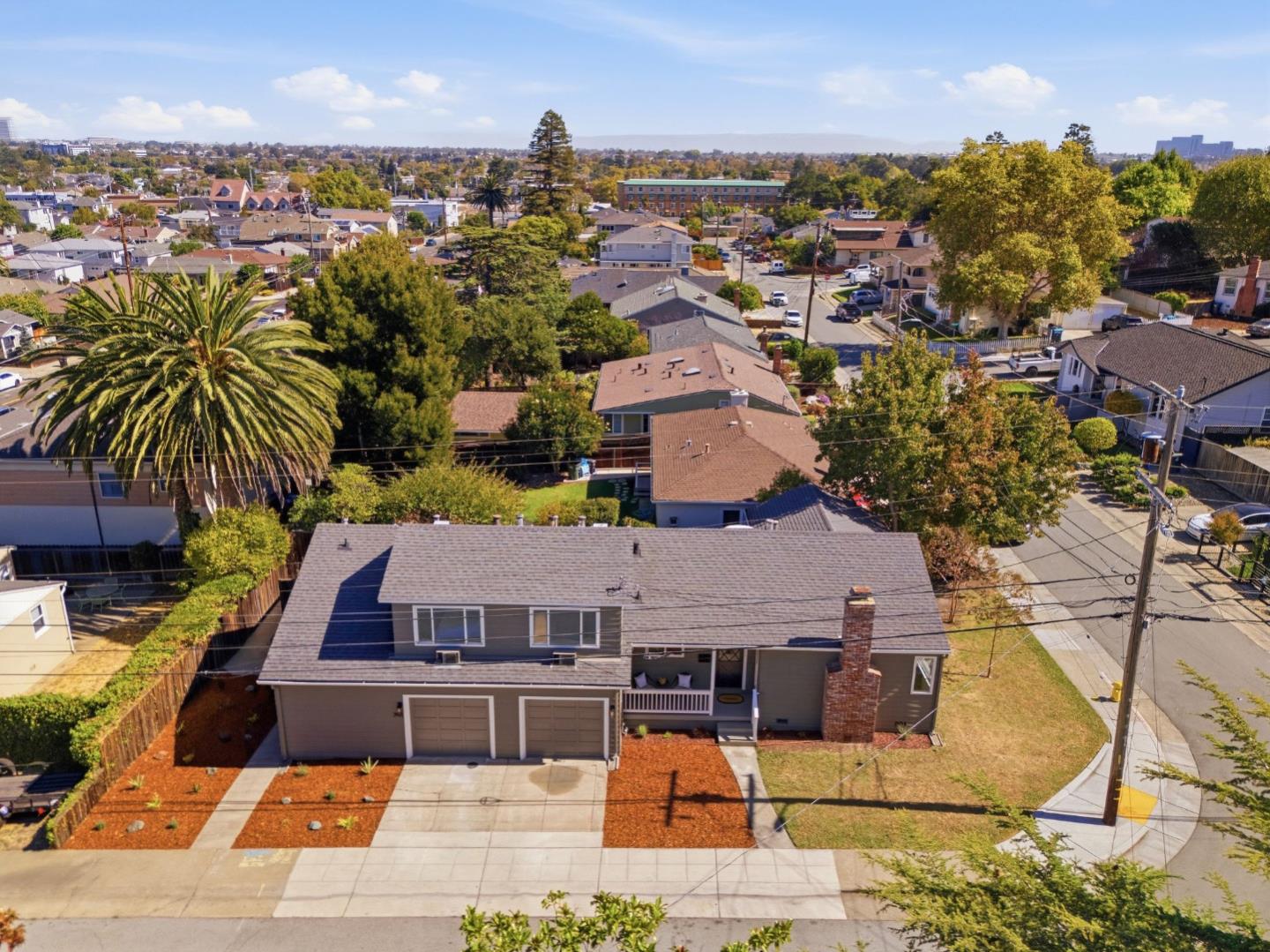 Aerial view of a gray single-story home with two garage doors, front landscaping, and surrounding San Mateo neighborhood.