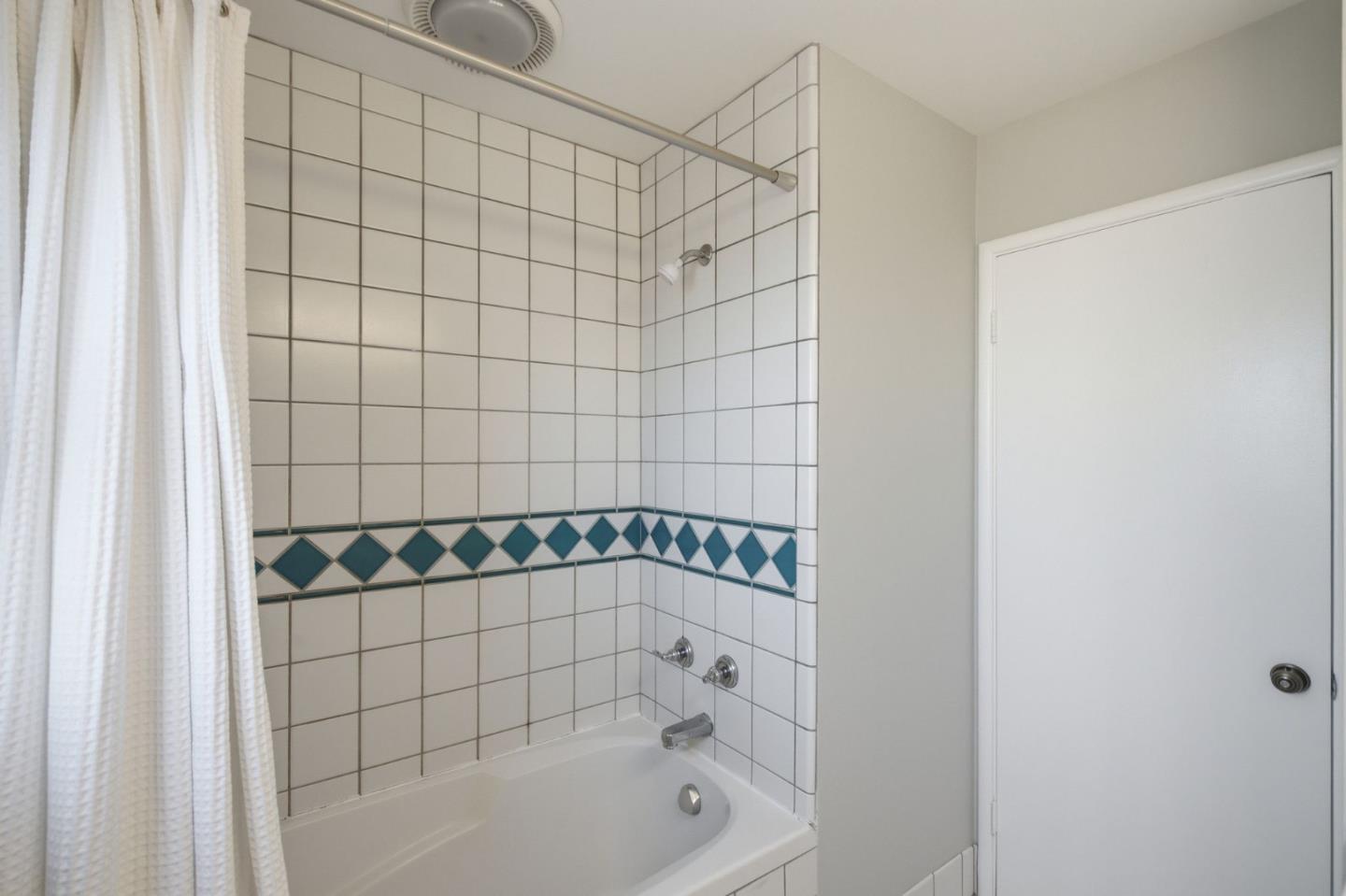 Bathroom with a white bathtub, tiled shower walls, and a teal diamond-pattern border.