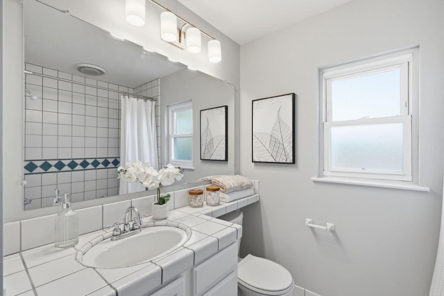 Bathroom with a tiled vanity, blue diamond shower accents, and framed botanical prints.