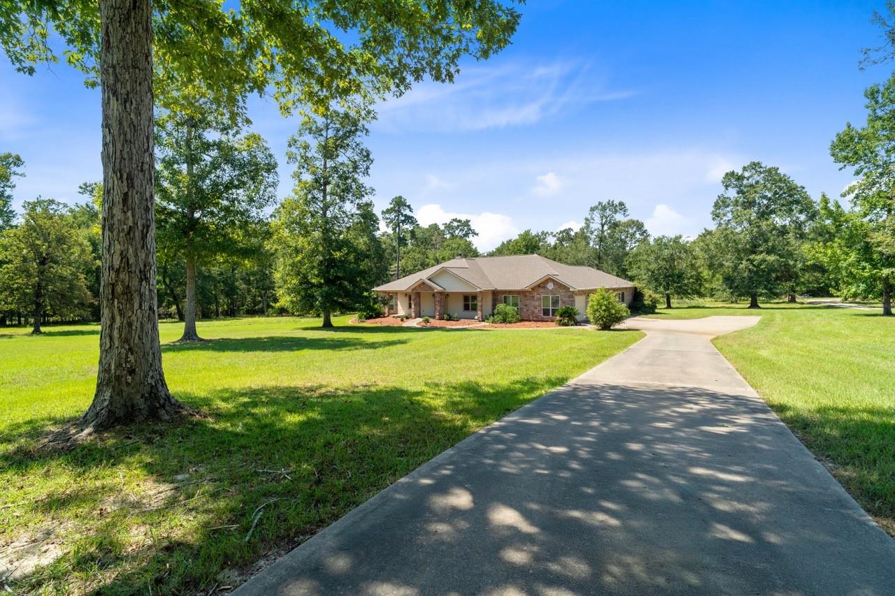 Single-story brick home set back from a curved driveway, surrounded by lawn and mature trees.