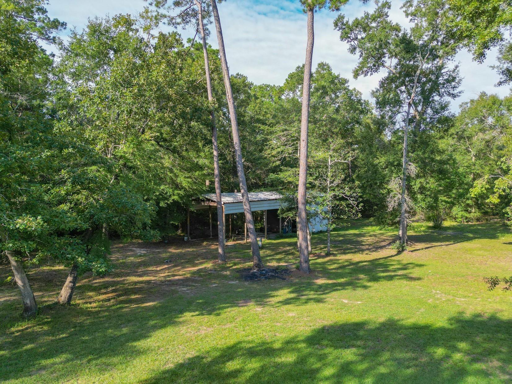 Wooded property with a grassy clearing and a small open-sided metal-roof shelter.