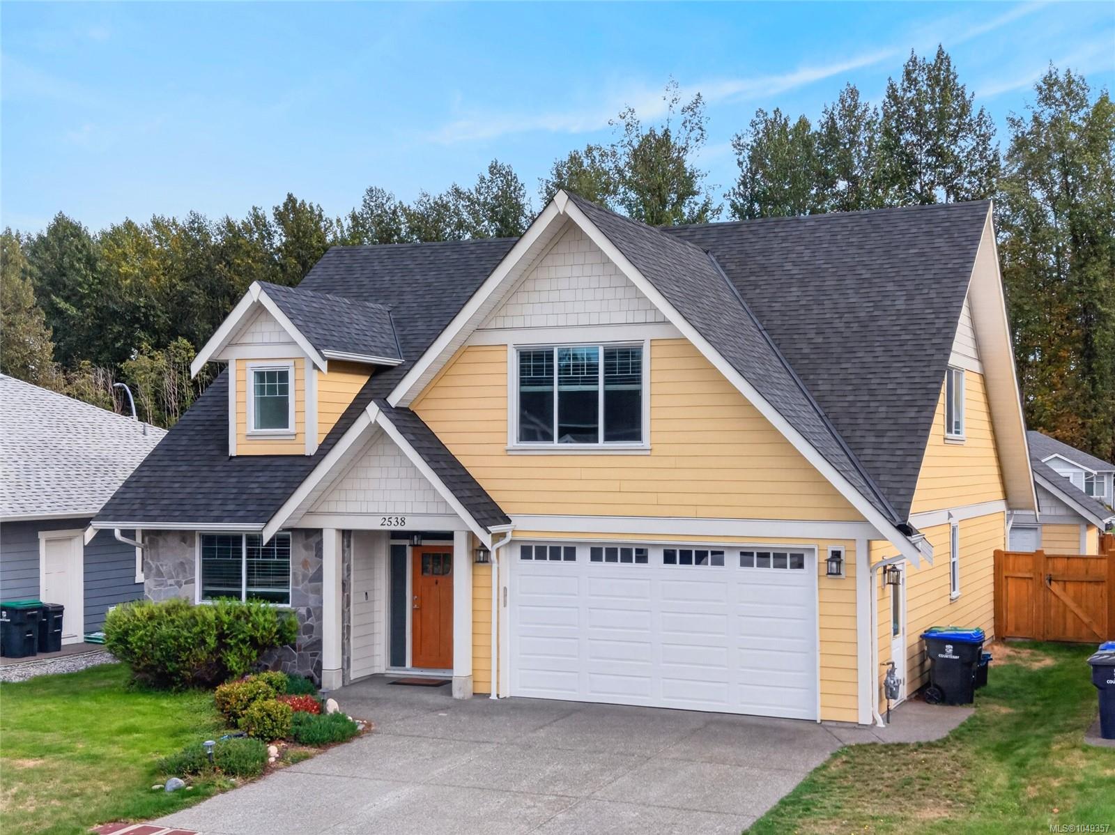 Yellow two-story house with steep gables, a double garage, and landscaped front yard.