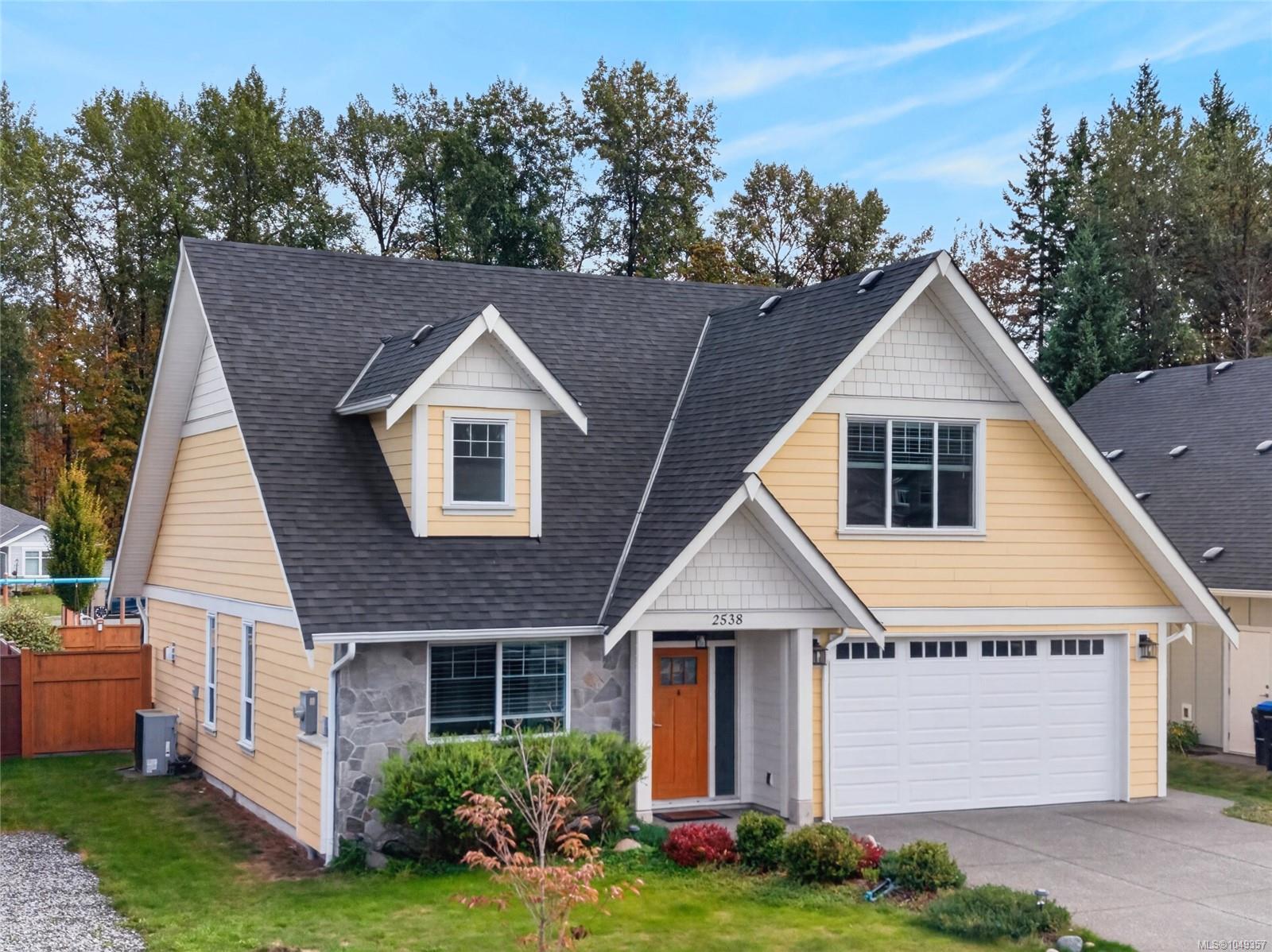 Yellow two-story house with steep dark roofs, stone facade, and attached double garage.