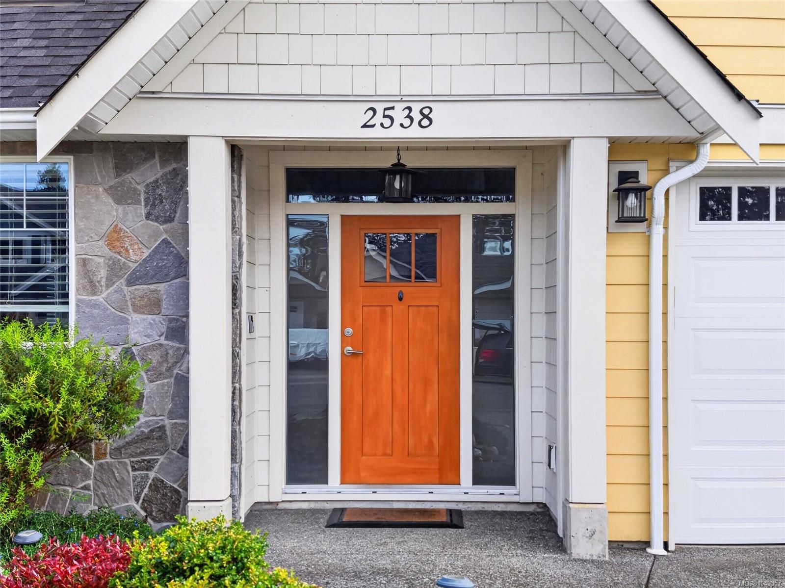 Home entrance with an orange wood door, white gabled porch, and the number 2538 above.
