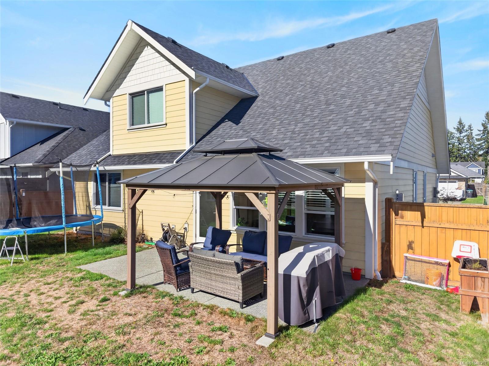 House rear patio with pergola-covered seating, a trampoline, and wooden fence.