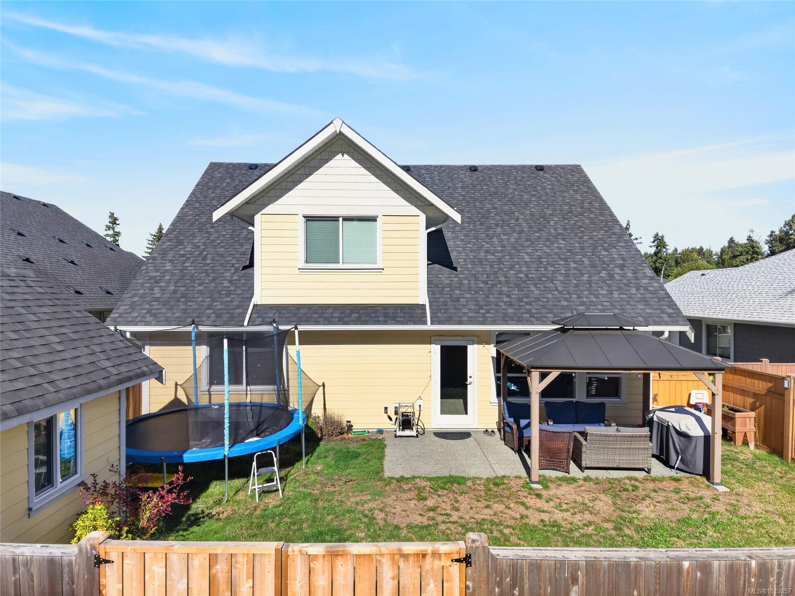 Yellow two-story home with a fenced backyard, trampoline, and covered patio with outdoor seating.