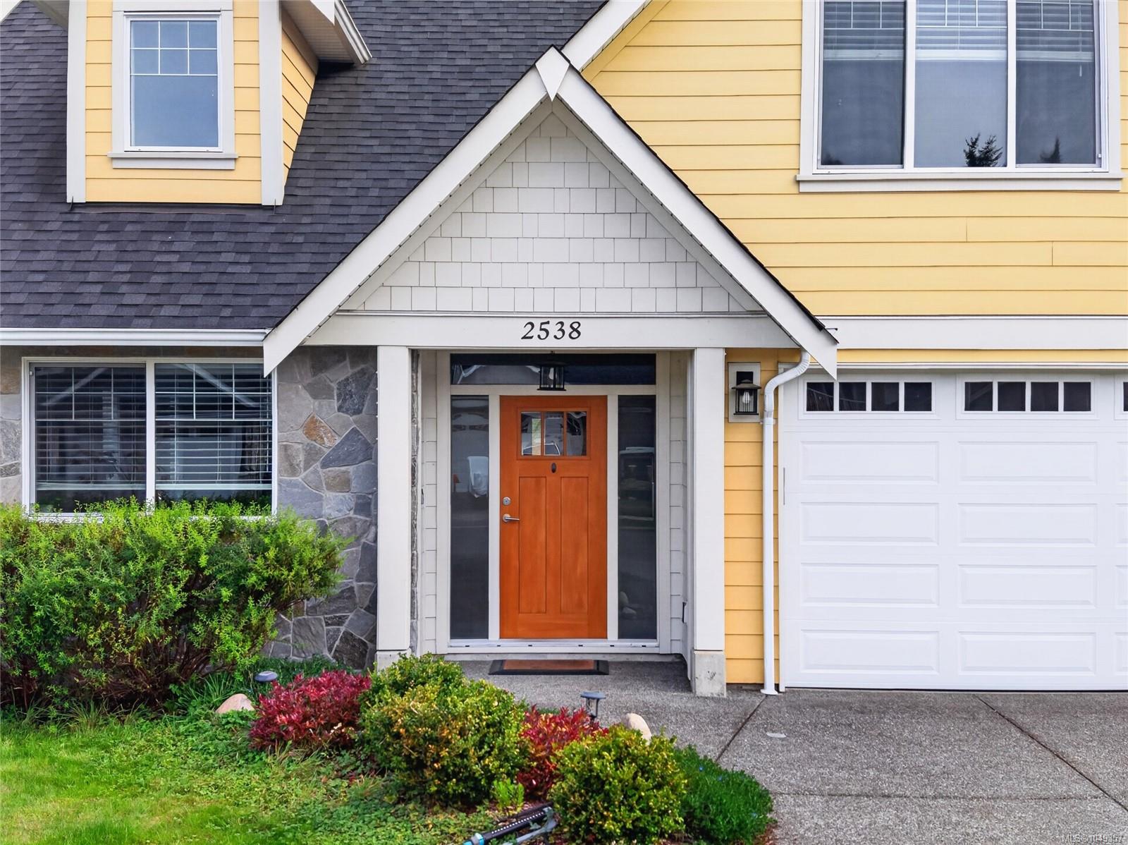 Front entrance of a yellow house with an orange door, stone accents, and an attached garage.