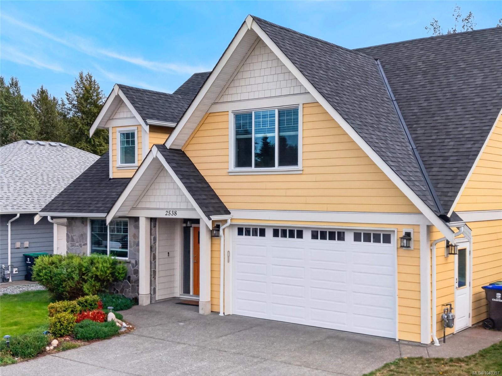 Yellow two-story house with steep gabled roofs, stone entry accents, and a white double garage.