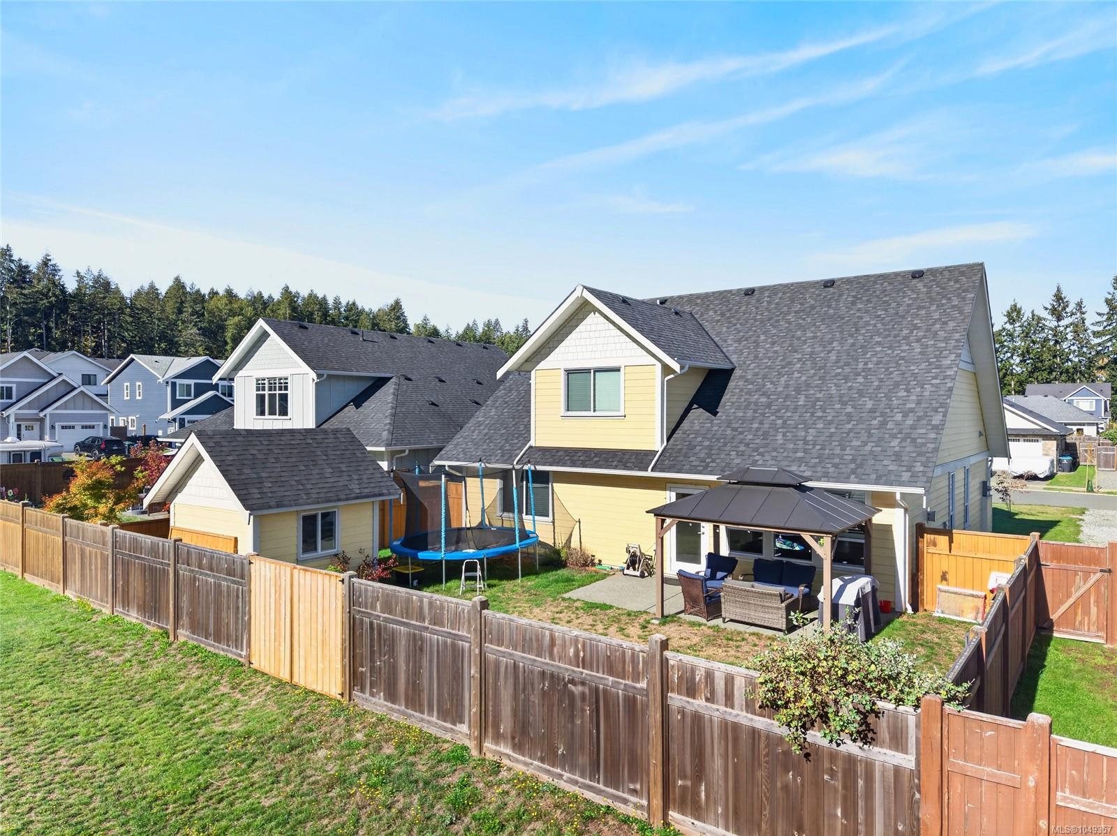 Yellow two-story home with a fenced backyard, covered patio, trampoline, and detached shed.