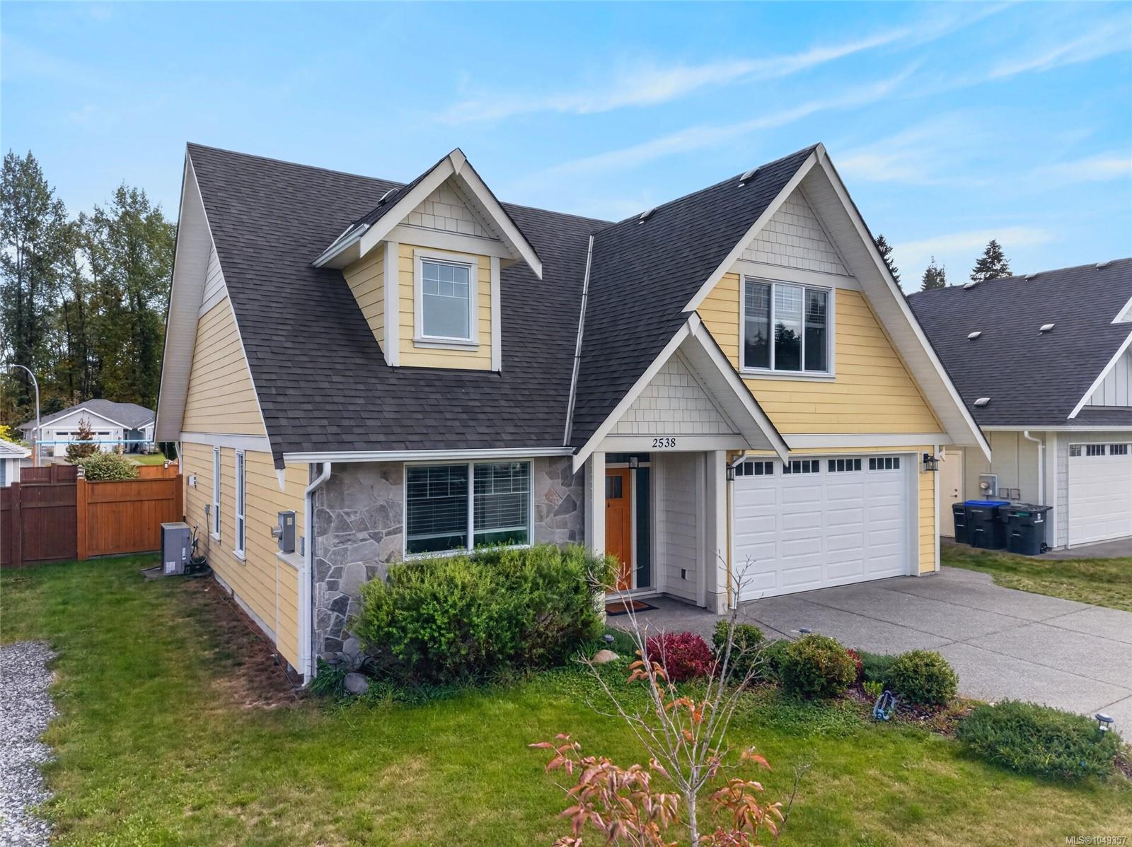 Yellow two-story house with gabled roofs, stone accents, and an attached double garage.