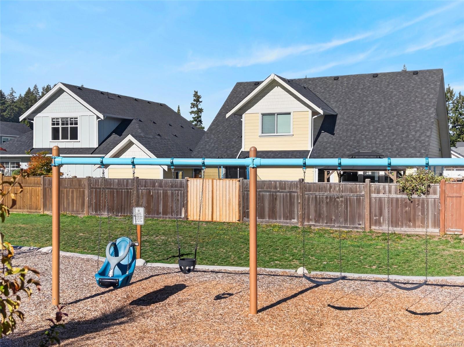 Residential homes behind a wooden fence, with a grassy yard and playground swings in the foreground.