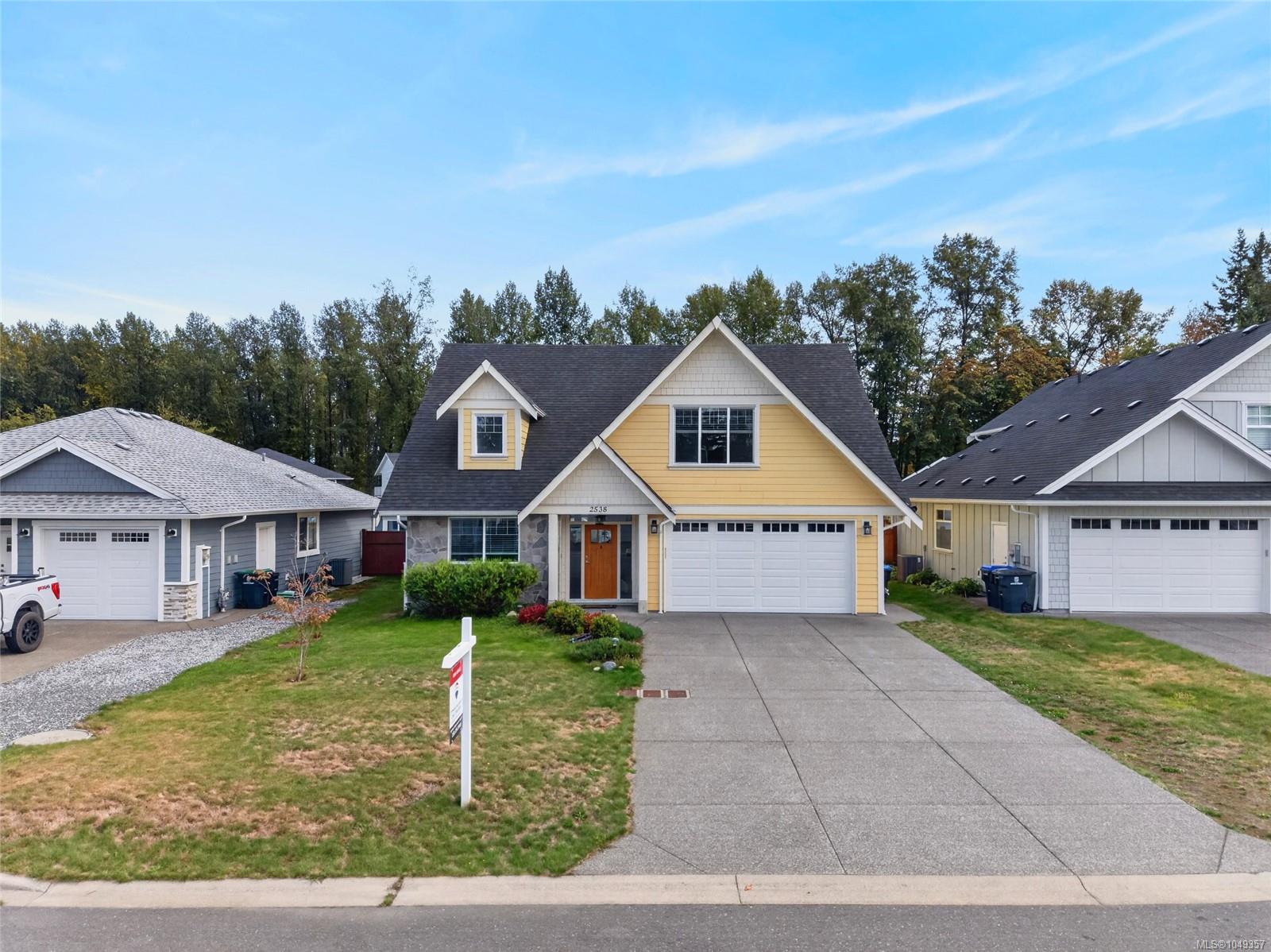 Yellow two-story house with a gabled roof, double garage, and wide concrete driveway.