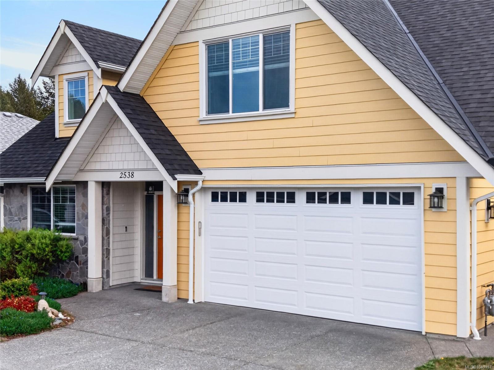 Yellow house with white trim, steep gables, stone entry, and a large double garage door.