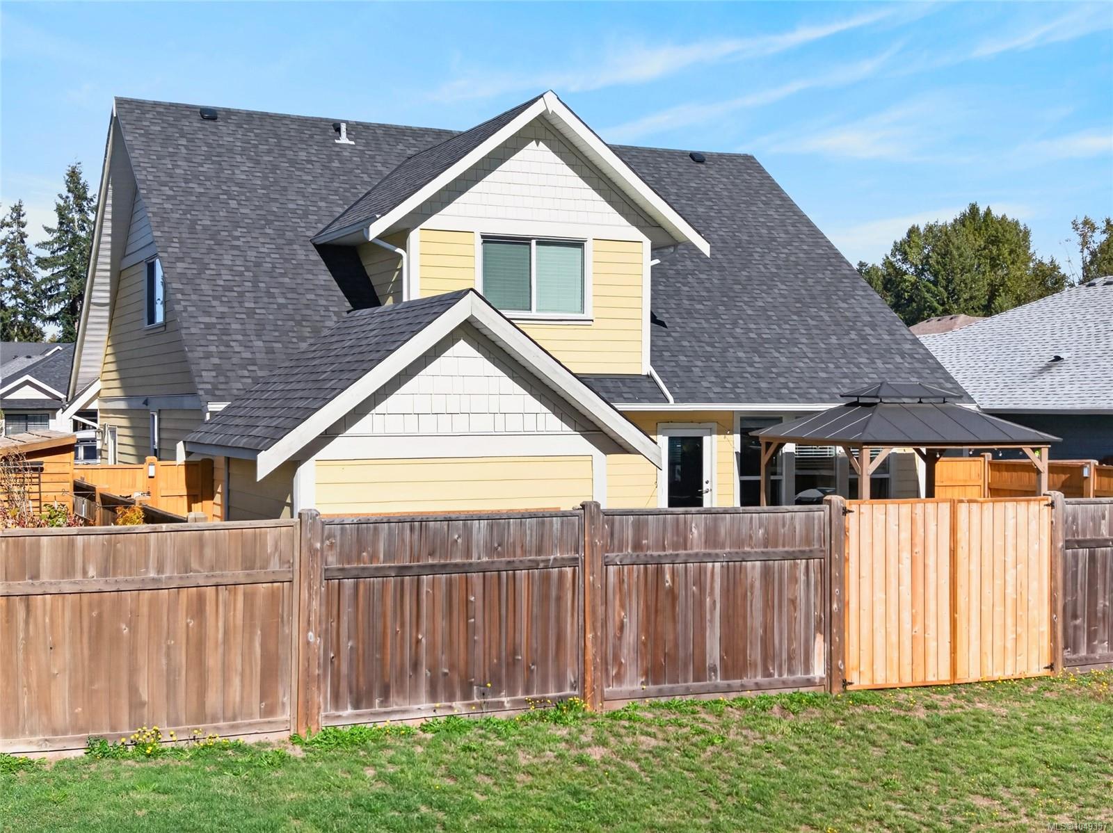 Yellow two-story house with multiple gables, a covered patio, and a tall wooden fence.