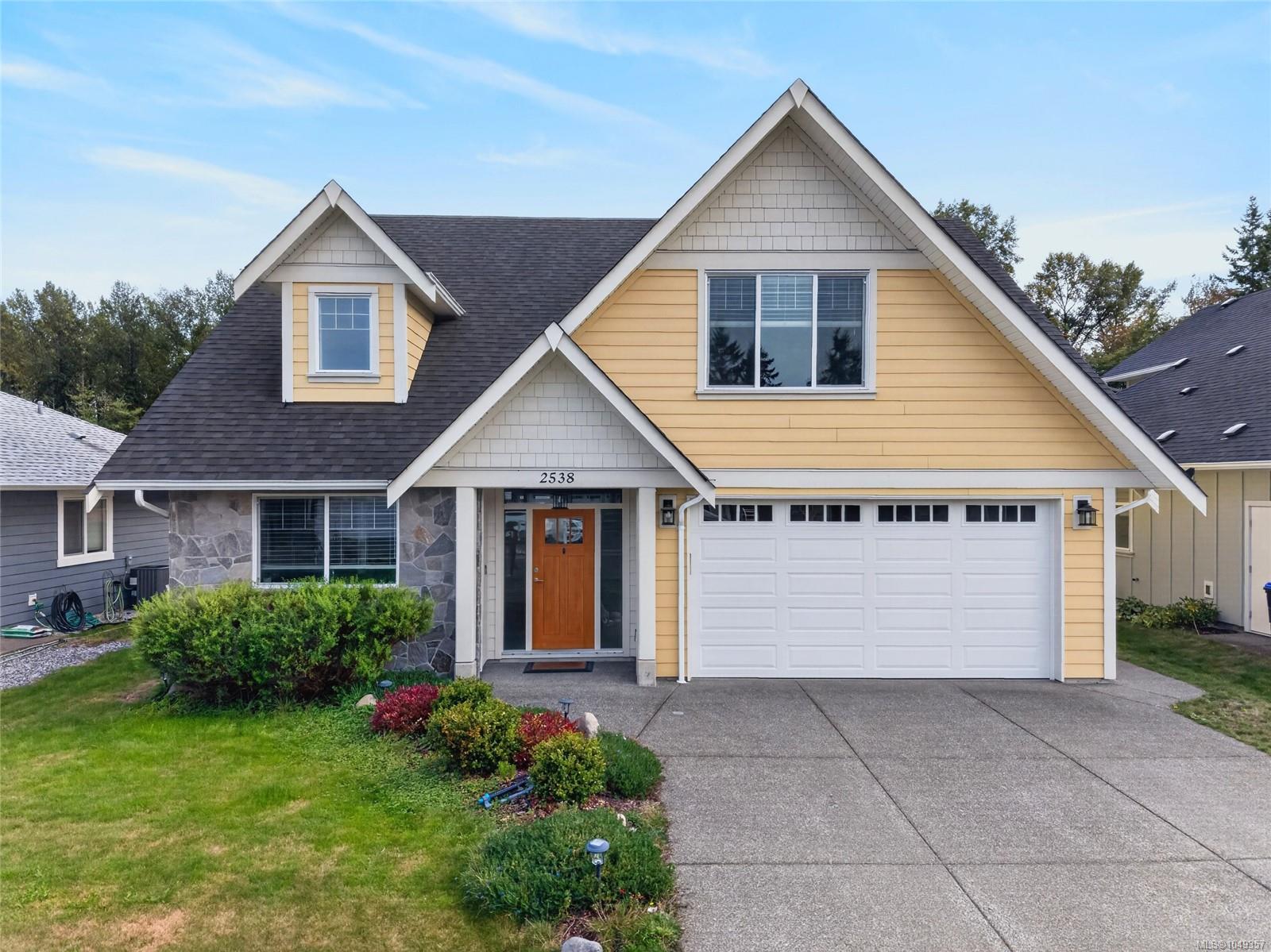 Yellow two-story house with steep gables, stone accents, and a white double garage.