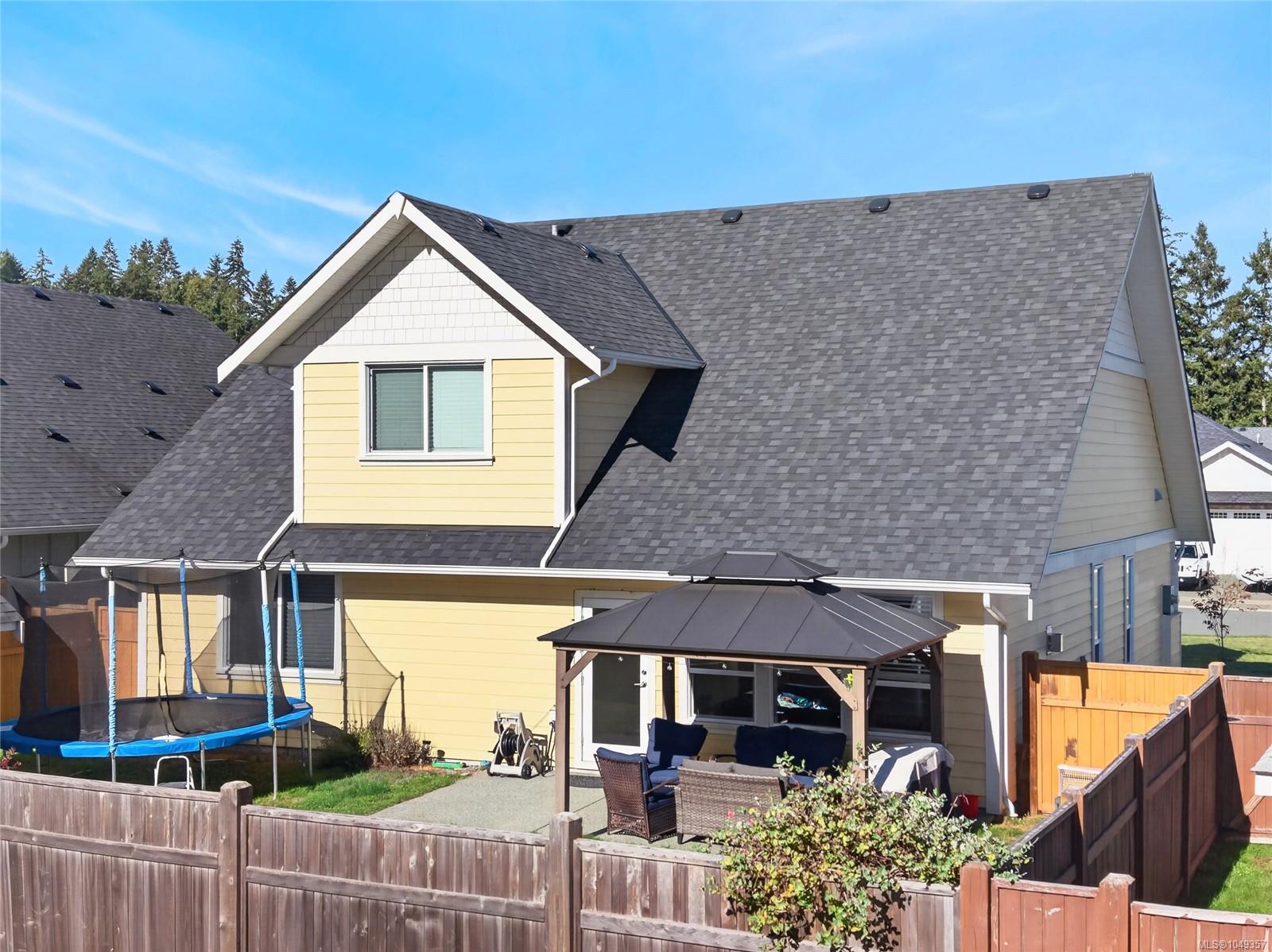 Yellow two-story house with a steep gray roof, fenced backyard, covered patio, and trampoline.