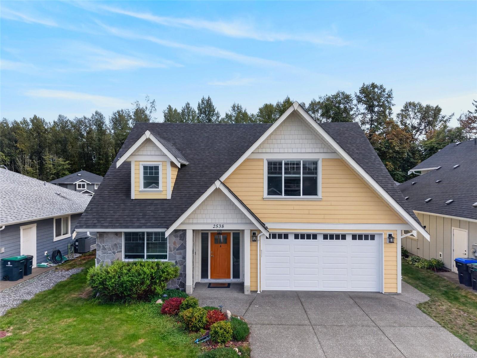 Yellow two-story house with stone accents, attached double garage, and landscaped front yard.