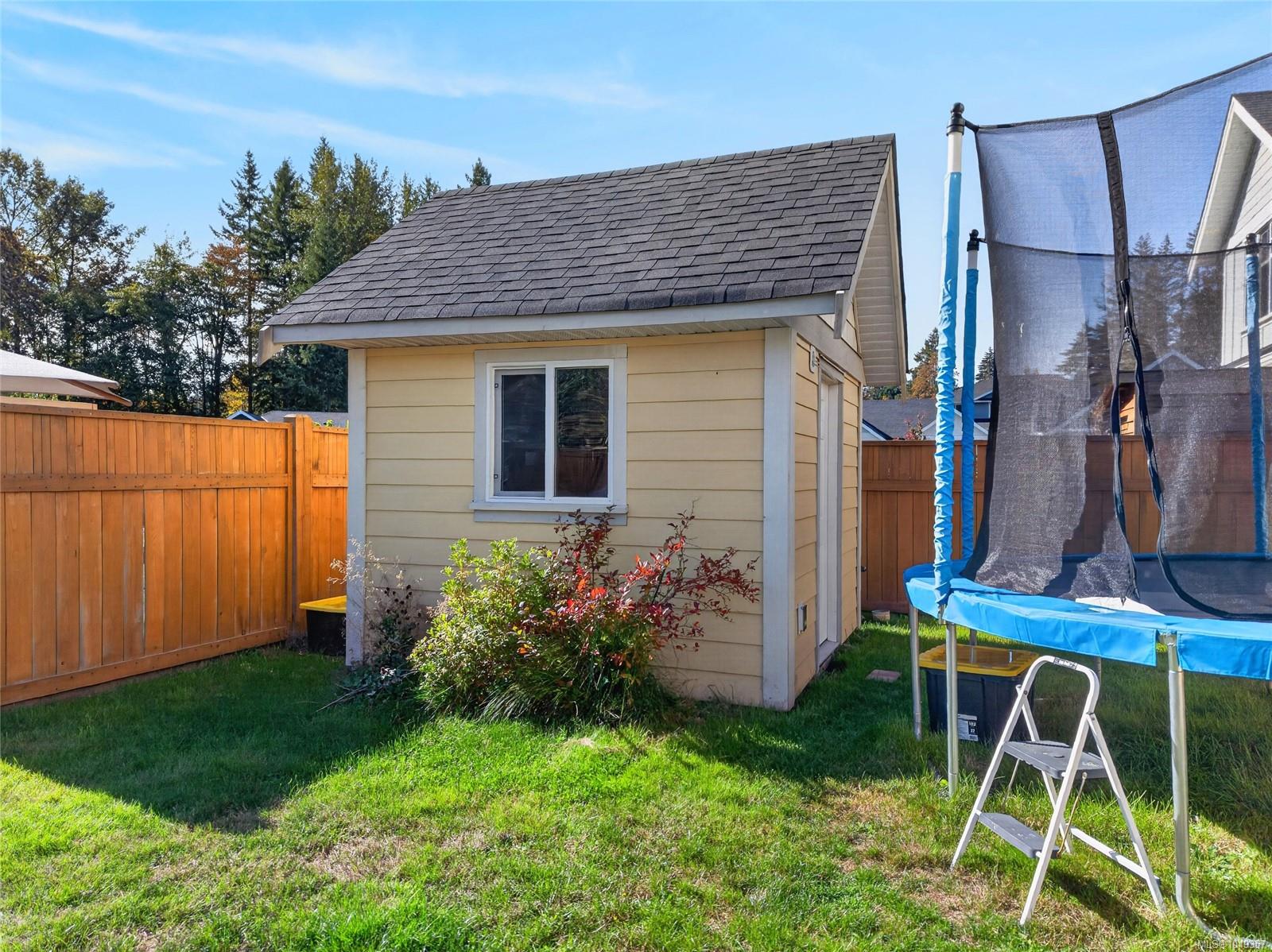 Backyard with a beige shed, wooden fencing, lawn, and trampoline.