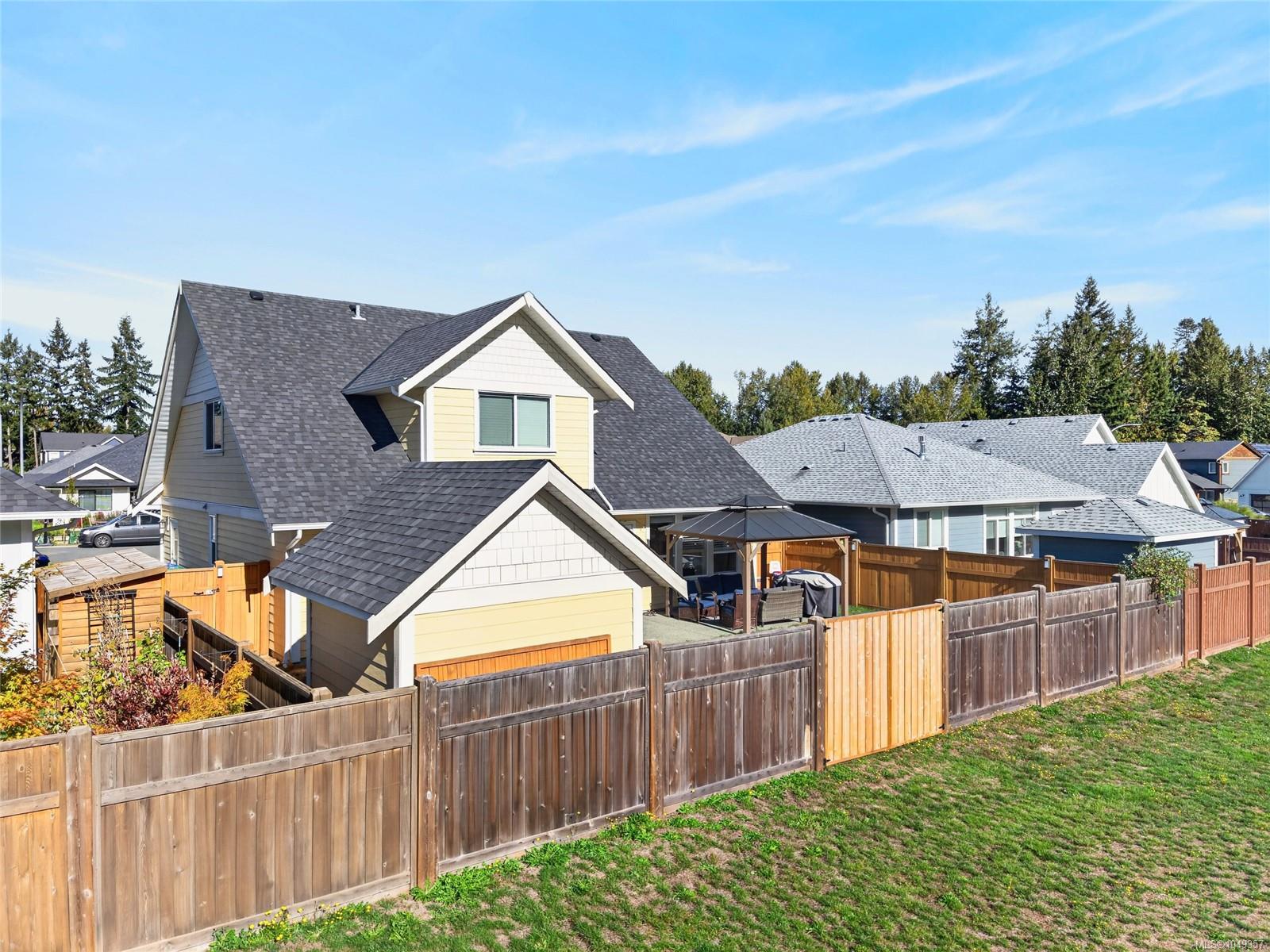 Rear exterior of a yellow house with a fenced yard, detached garage, and covered patio.