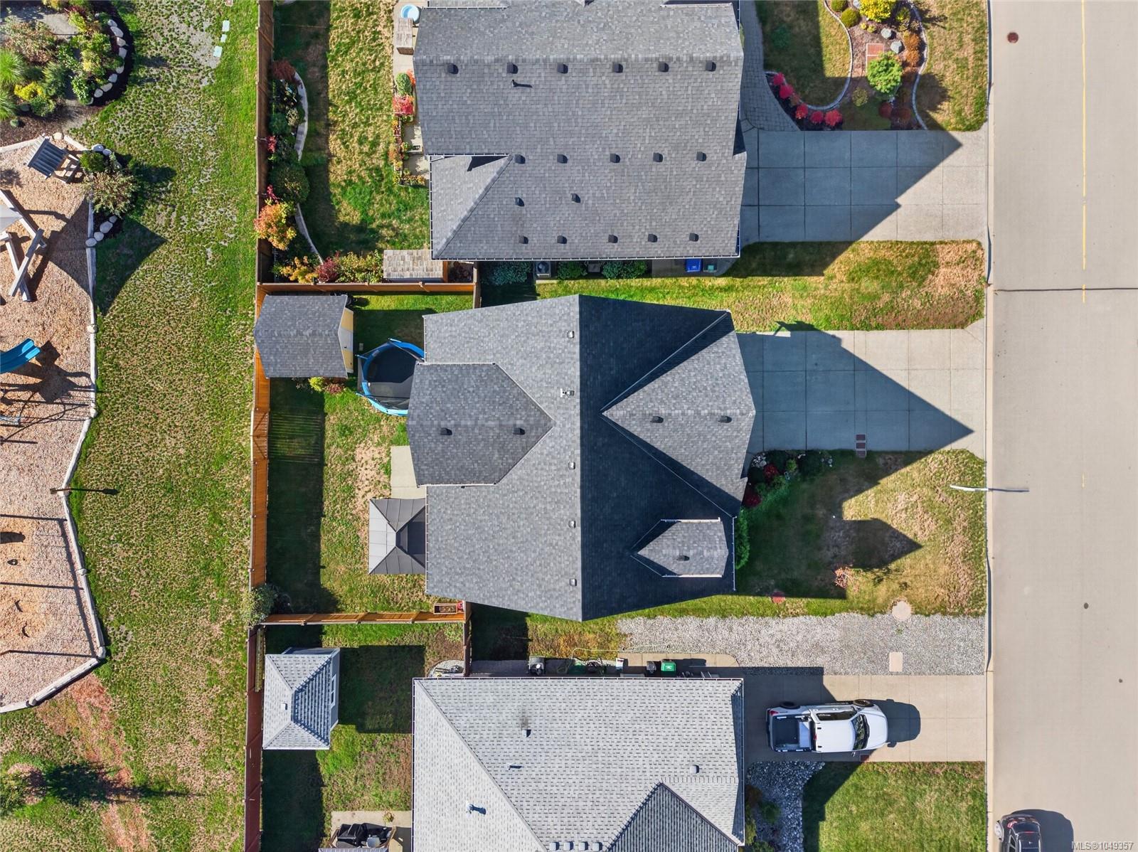 Aerial view of a gray-roofed home with a fenced backyard beside the street.