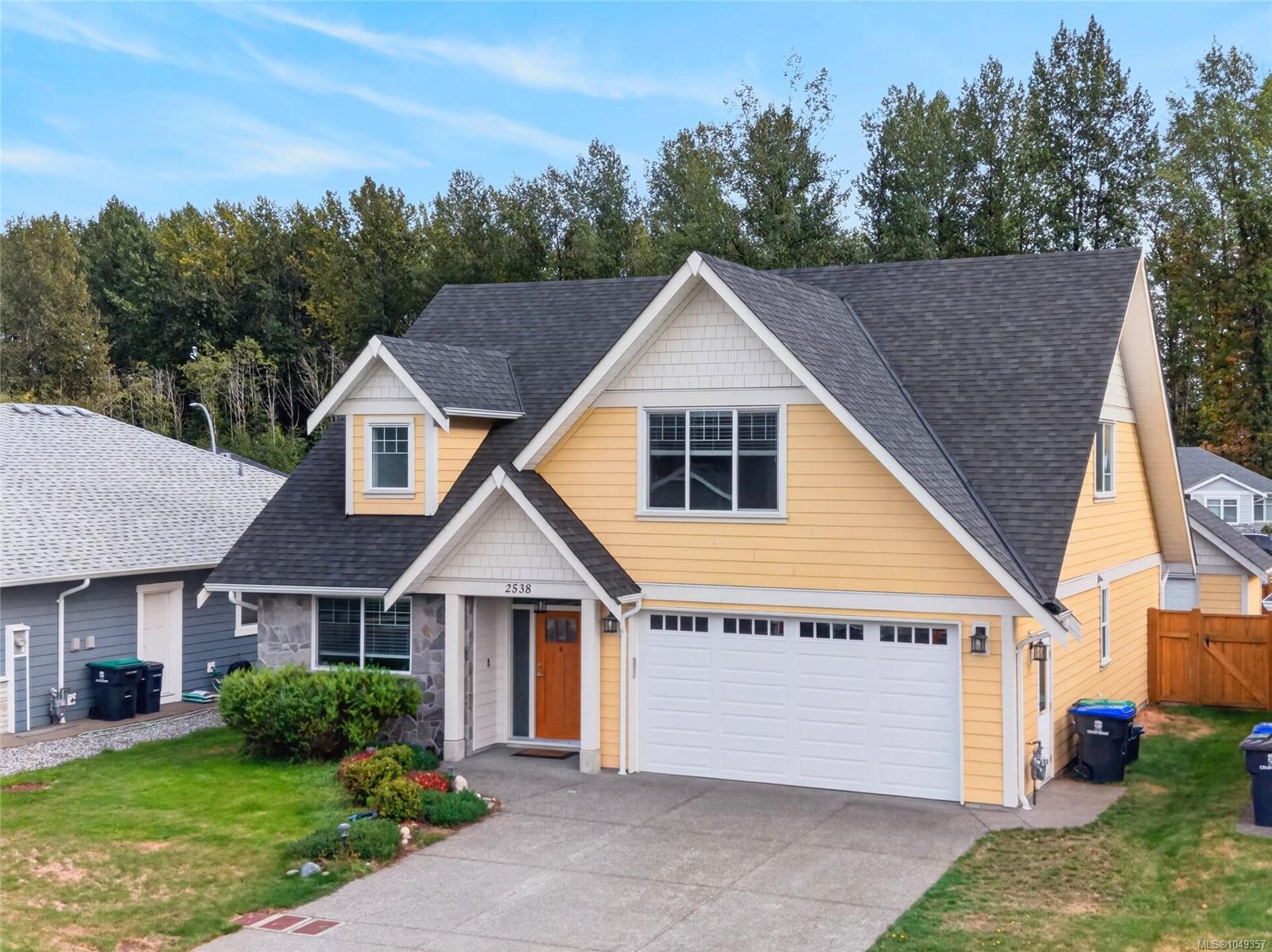 Yellow gabled house with a double garage, stone entry accents, and a landscaped front yard.