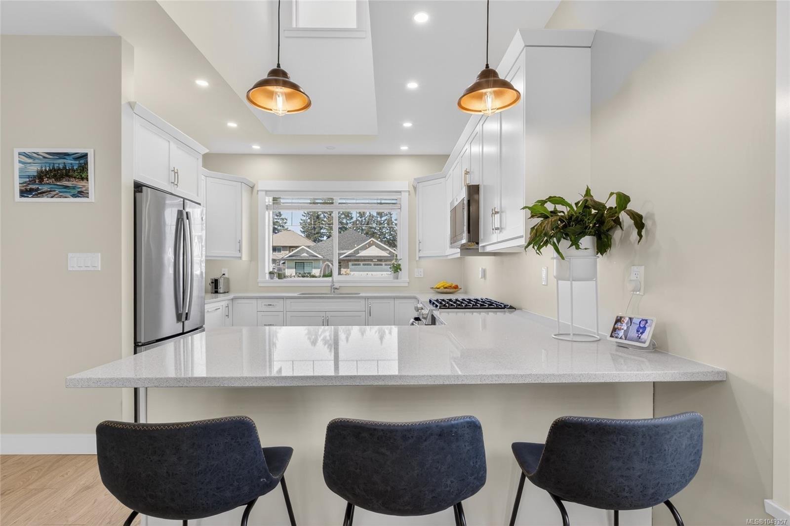 Bright kitchen with white cabinets, stainless steel appliances, and a large island with three bar stools.