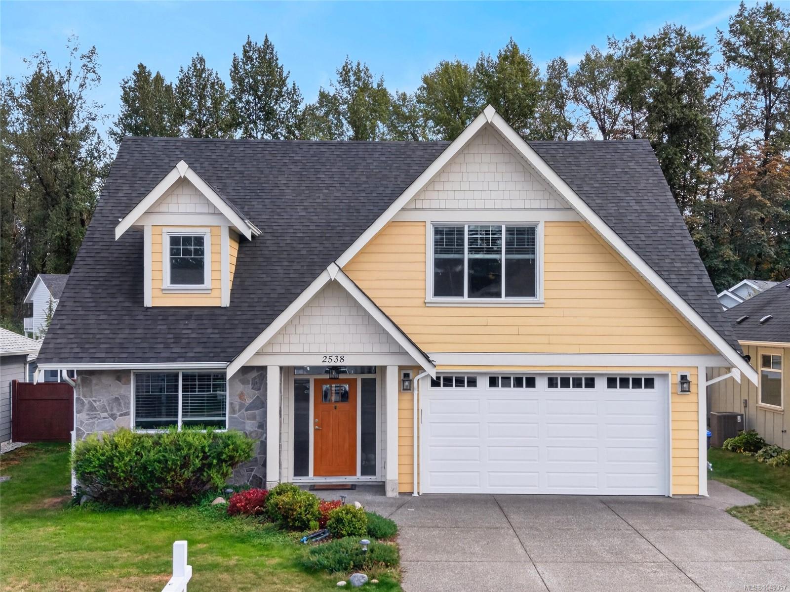 Yellow two-story house with steep gables, stone accents, and an attached double garage.