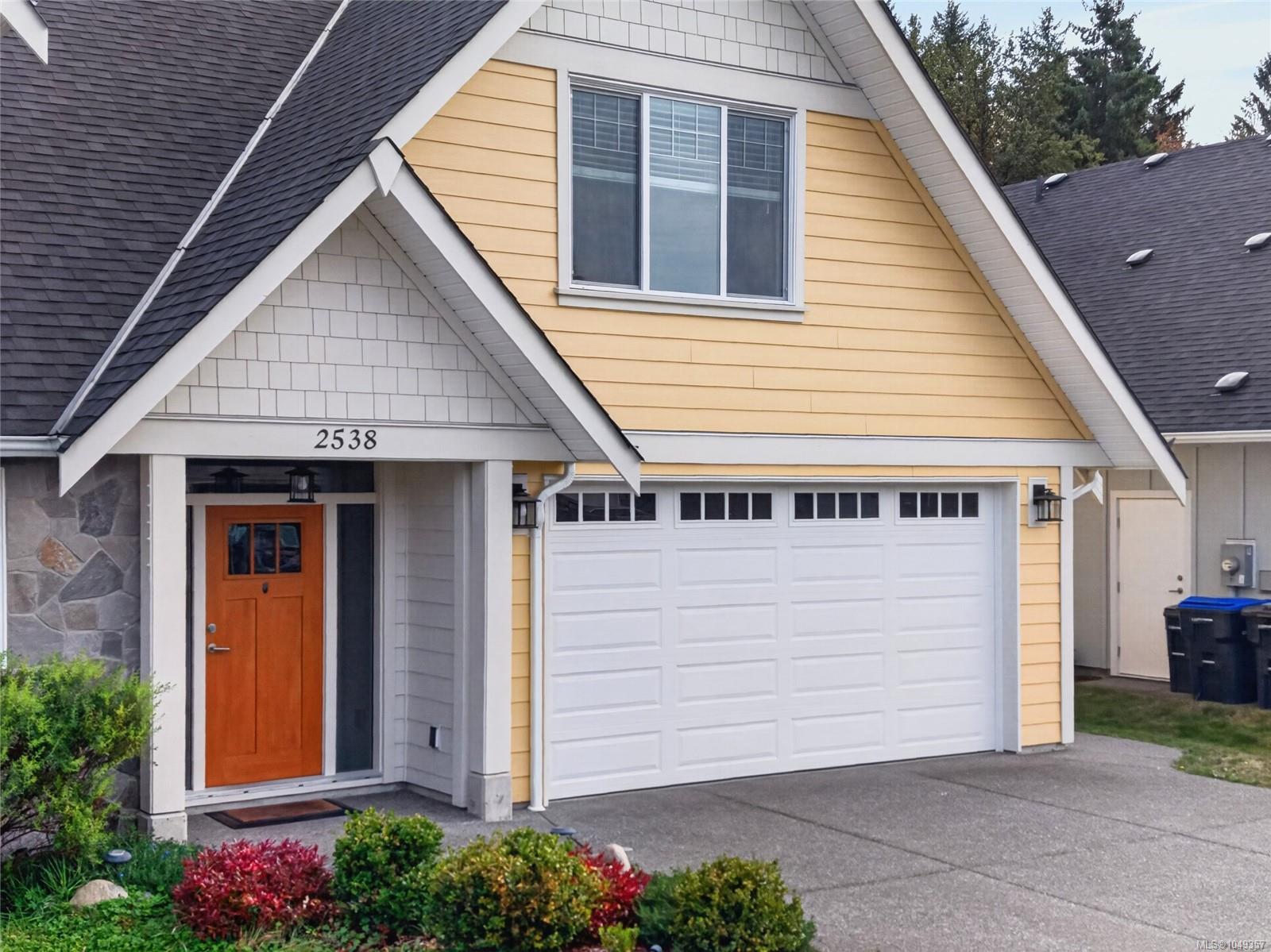 Yellow two-story house with an orange front door, stone accent wall, and white double garage door.