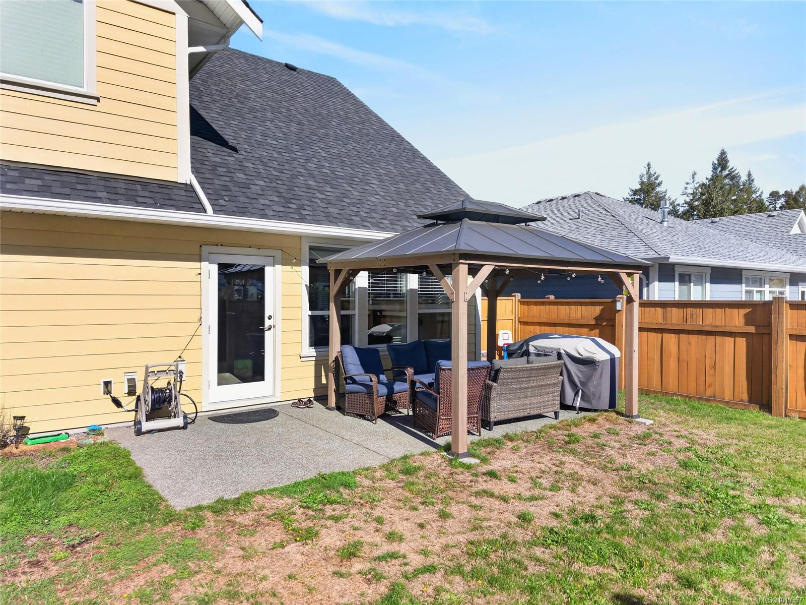 House’s rear patio with a covered pavilion, wicker seating, barbecue, and fenced yard.