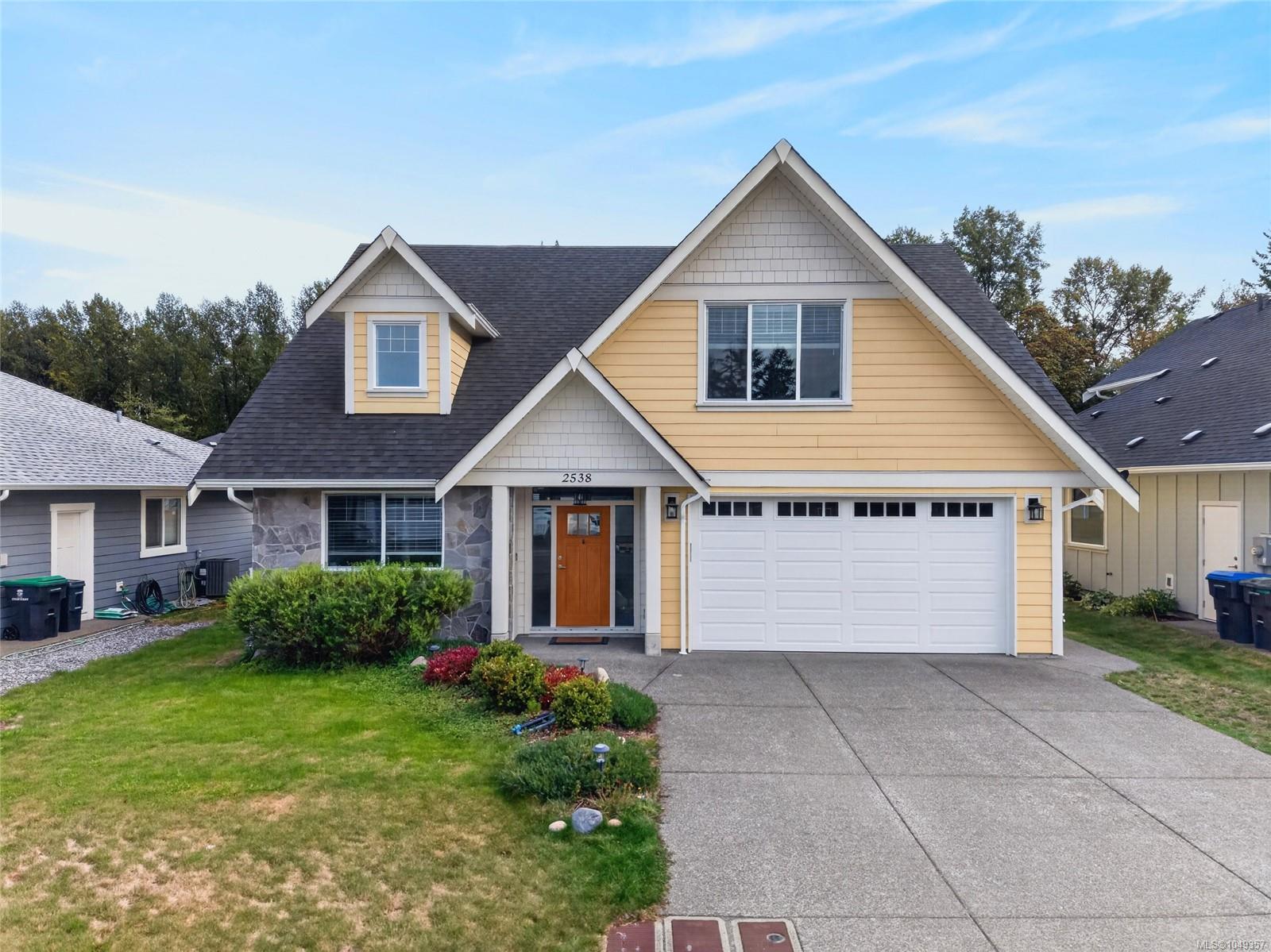 Yellow gabled house with stone accents, attached double garage, and landscaped front lawn.