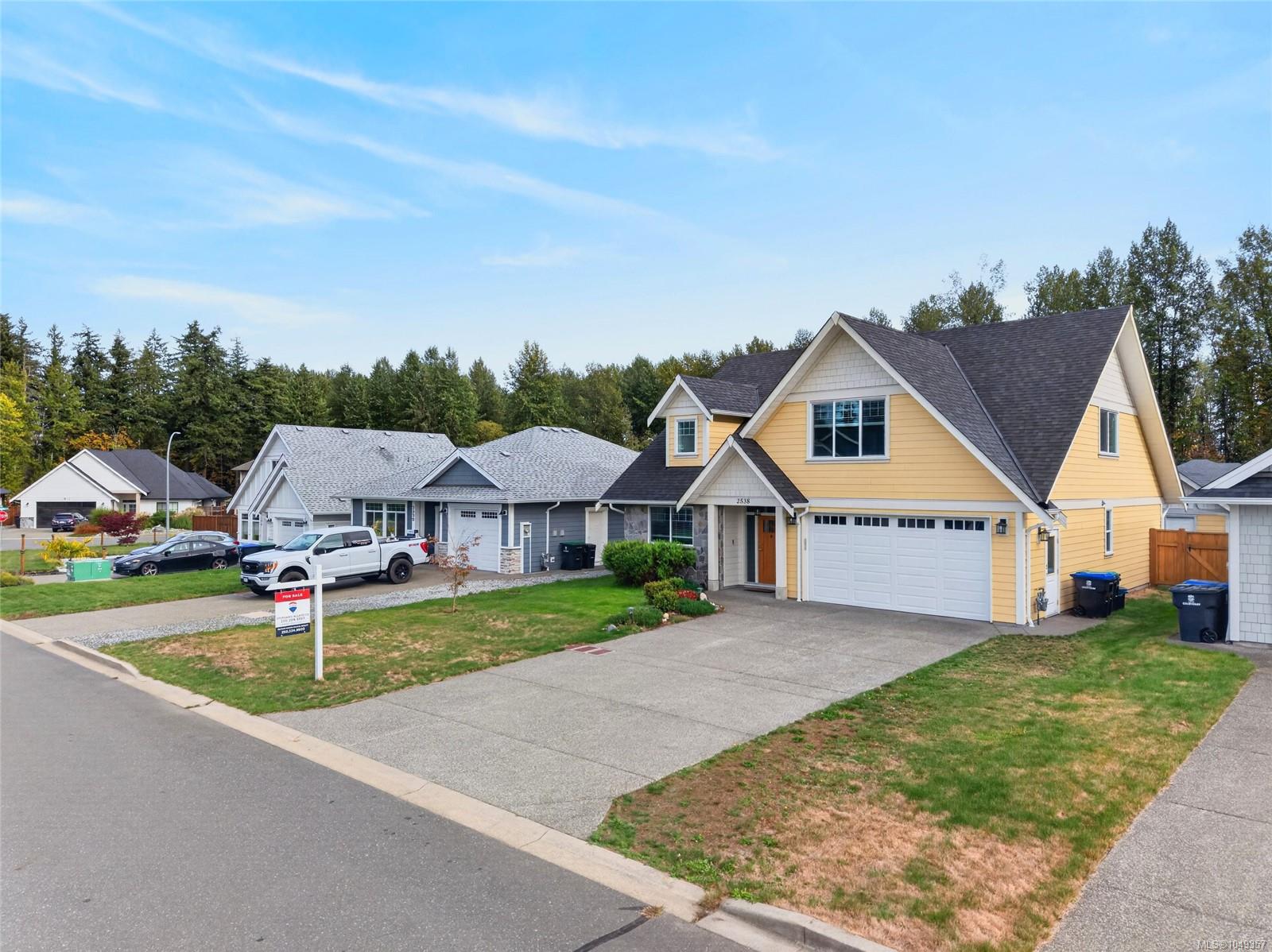 Yellow two-story house with an attached double garage and a for-sale sign on the lawn.