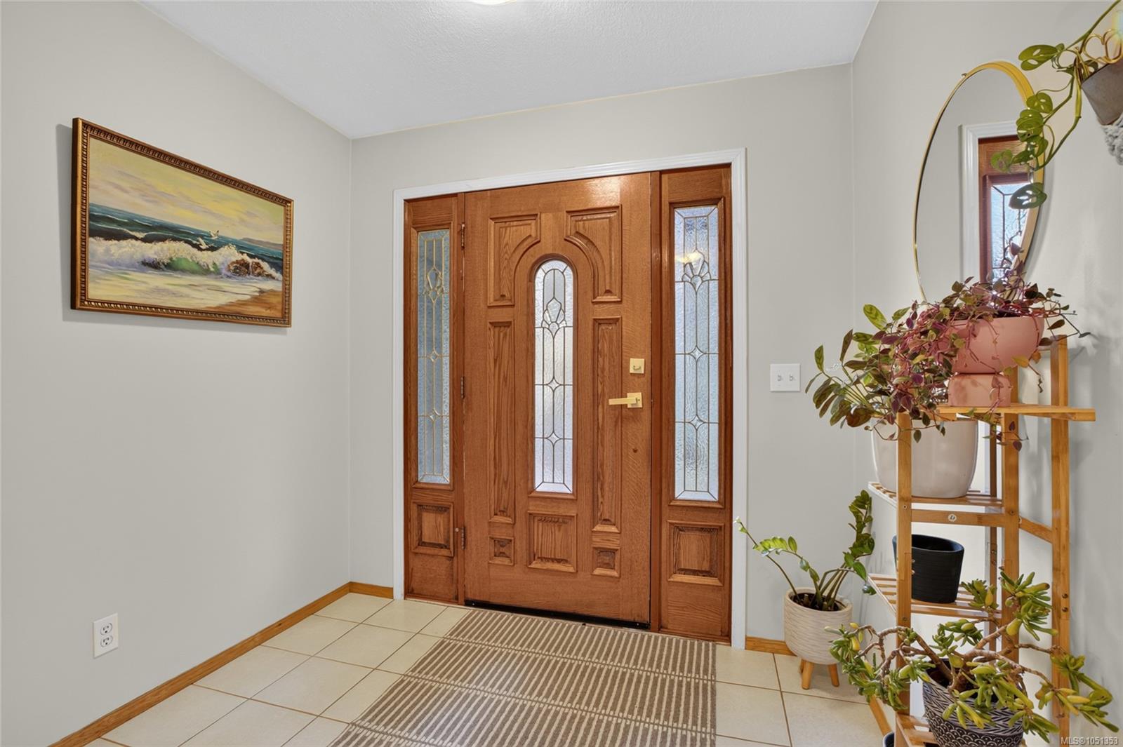 Entry foyer with a carved wood front door, stained-glass panels, tiled floor, potted plants, and coastal painting.