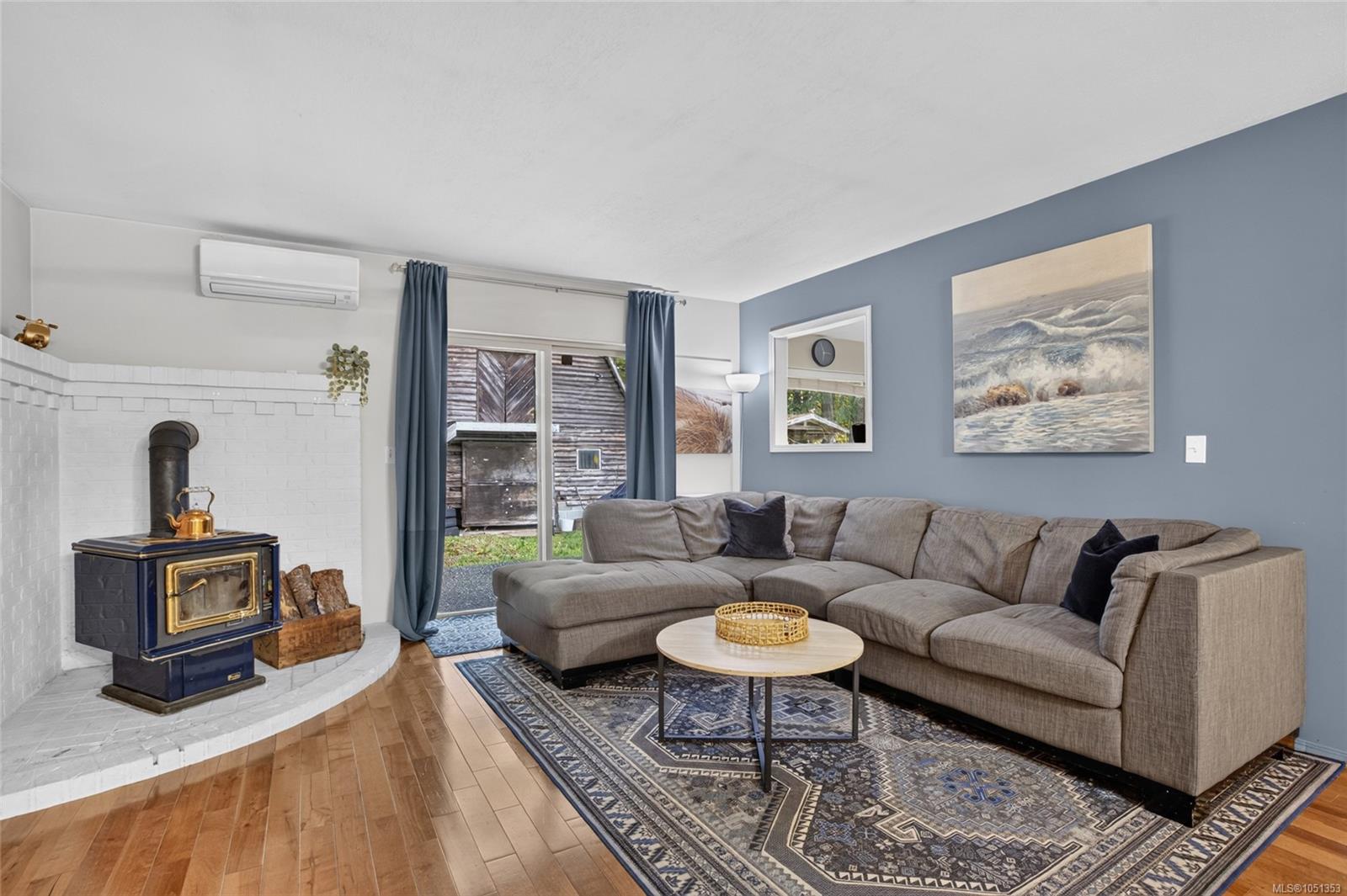 Living room with a gray sectional sofa and a brass-trimmed wood stove in a white brick surround.
