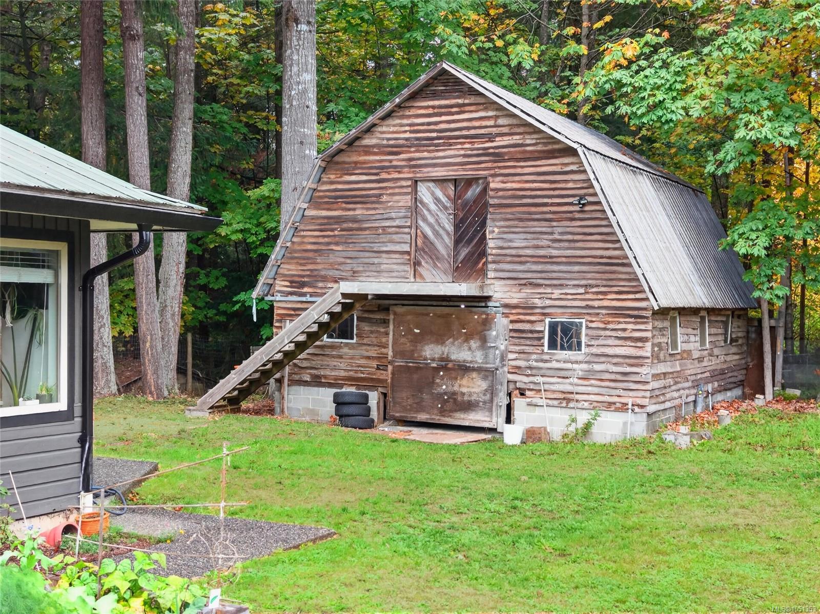 Weathered wooden barn with a gambrel roof and exterior staircase in a tree-lined yard.