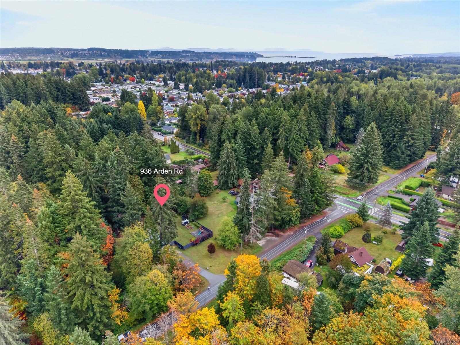 Aerial view of 936 Arden Rd, a wooded property with a clearing, homes, and distant water.