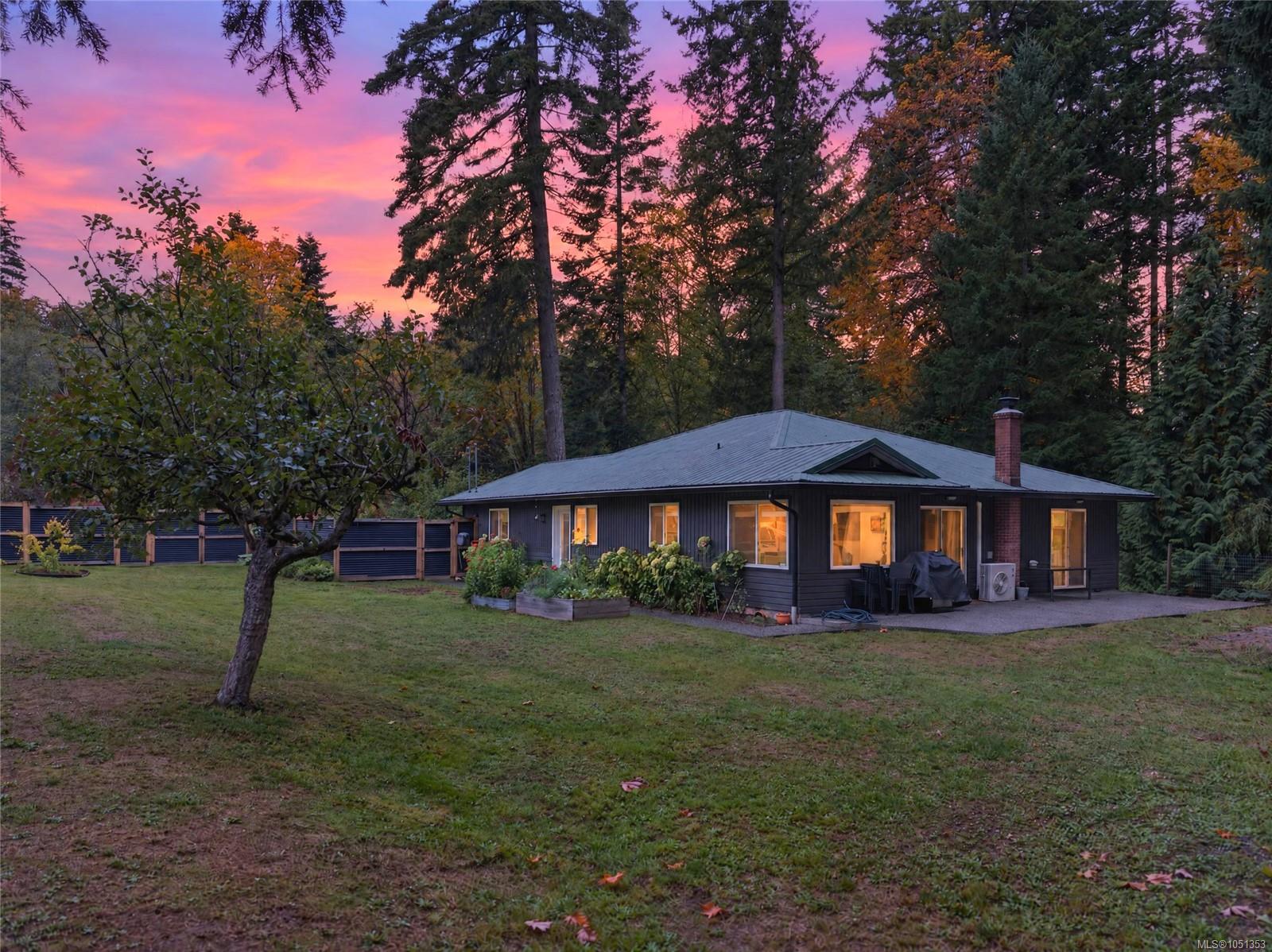 Single-story home with a patio in a wooded yard beneath a vivid pink dusk sky.