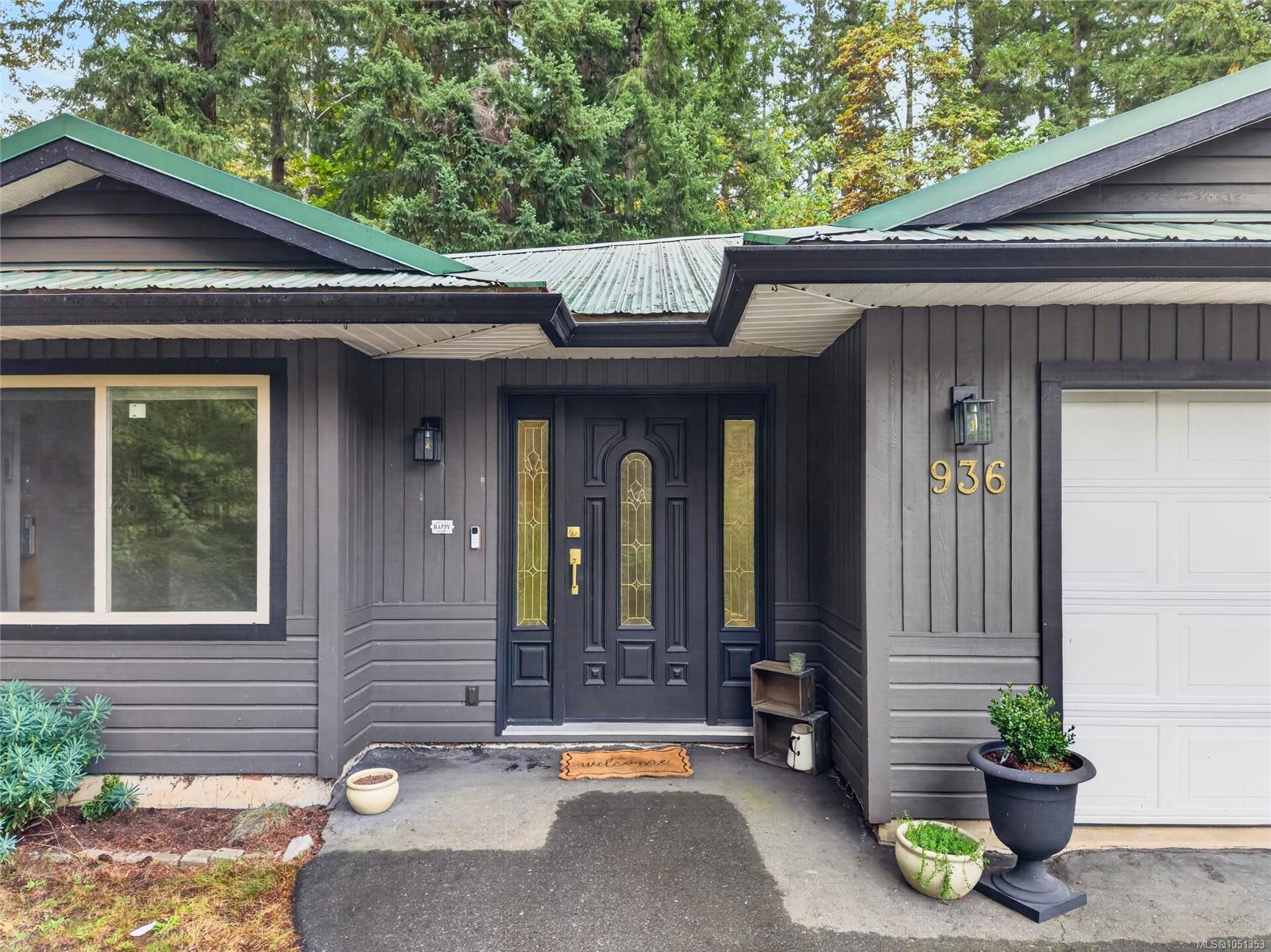 Home entrance with dark siding, decorative black door, green roof, and gold 936 address numbers.