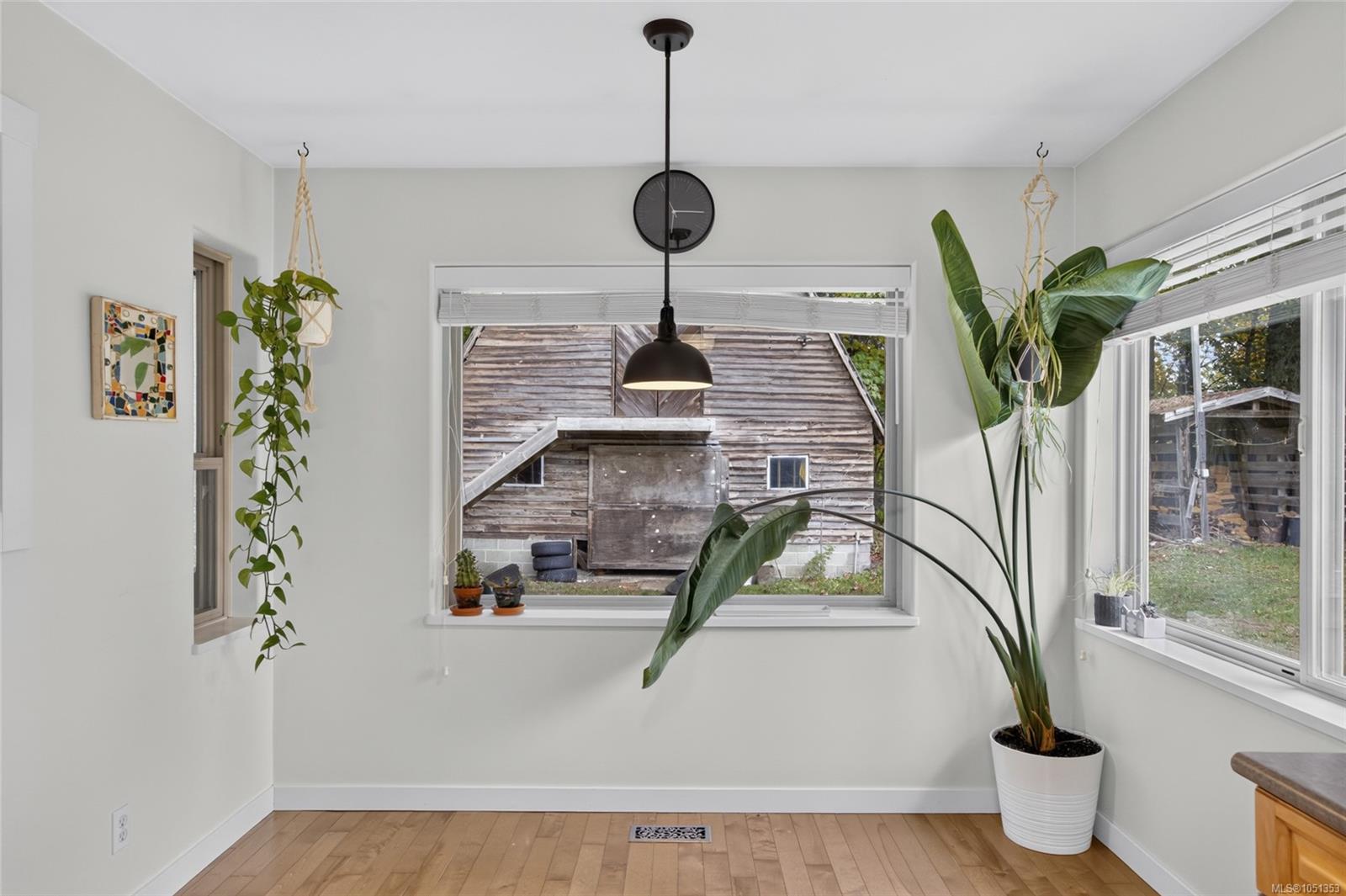 Bright room with large windows, wood flooring, a black pendant light, and potted plants.