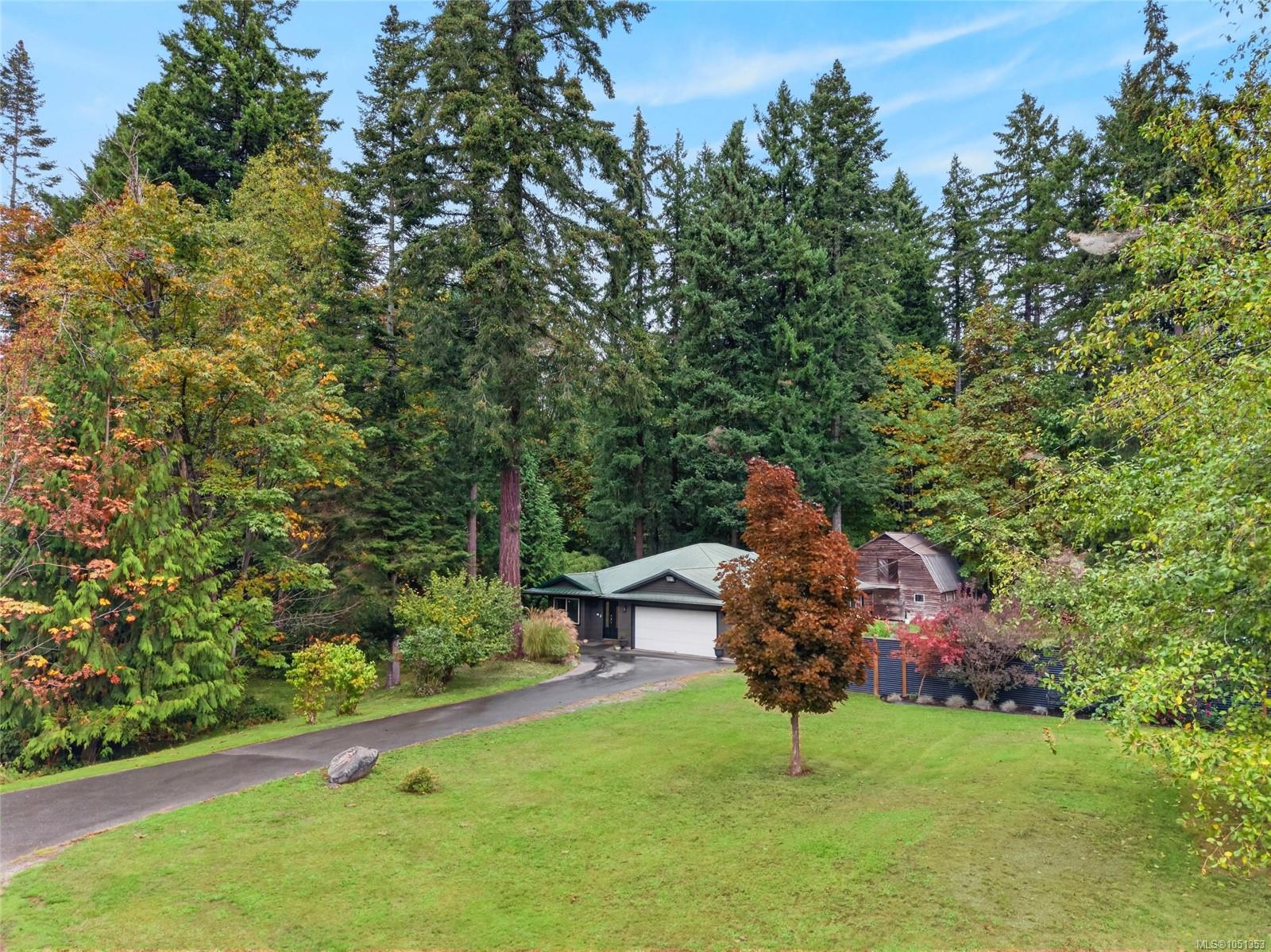 House with an attached garage nestled among tall evergreens and autumn foliage, beside a curving driveway.