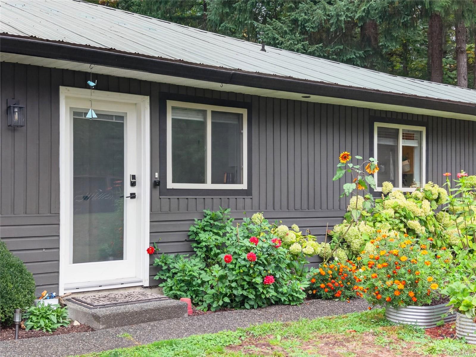 Dark gray house entrance with white door and windows beside a colorful flower garden.