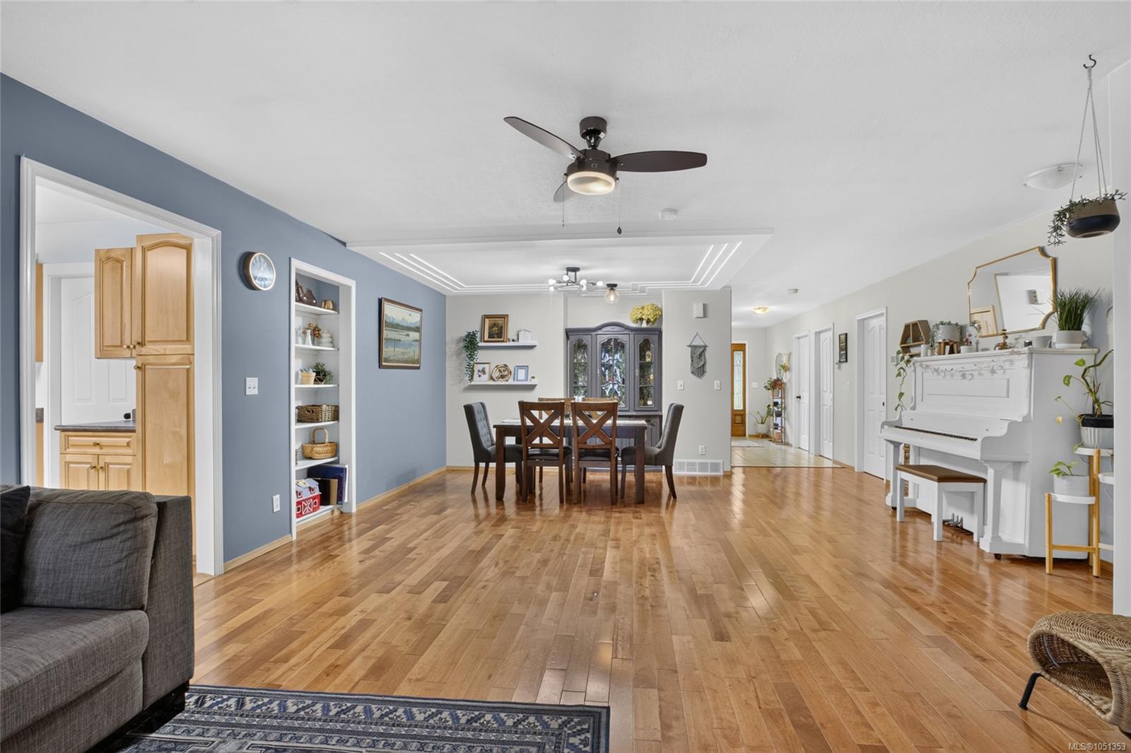 Open living and dining room with hardwood floors, blue accent wall, built-in shelves, and white piano.