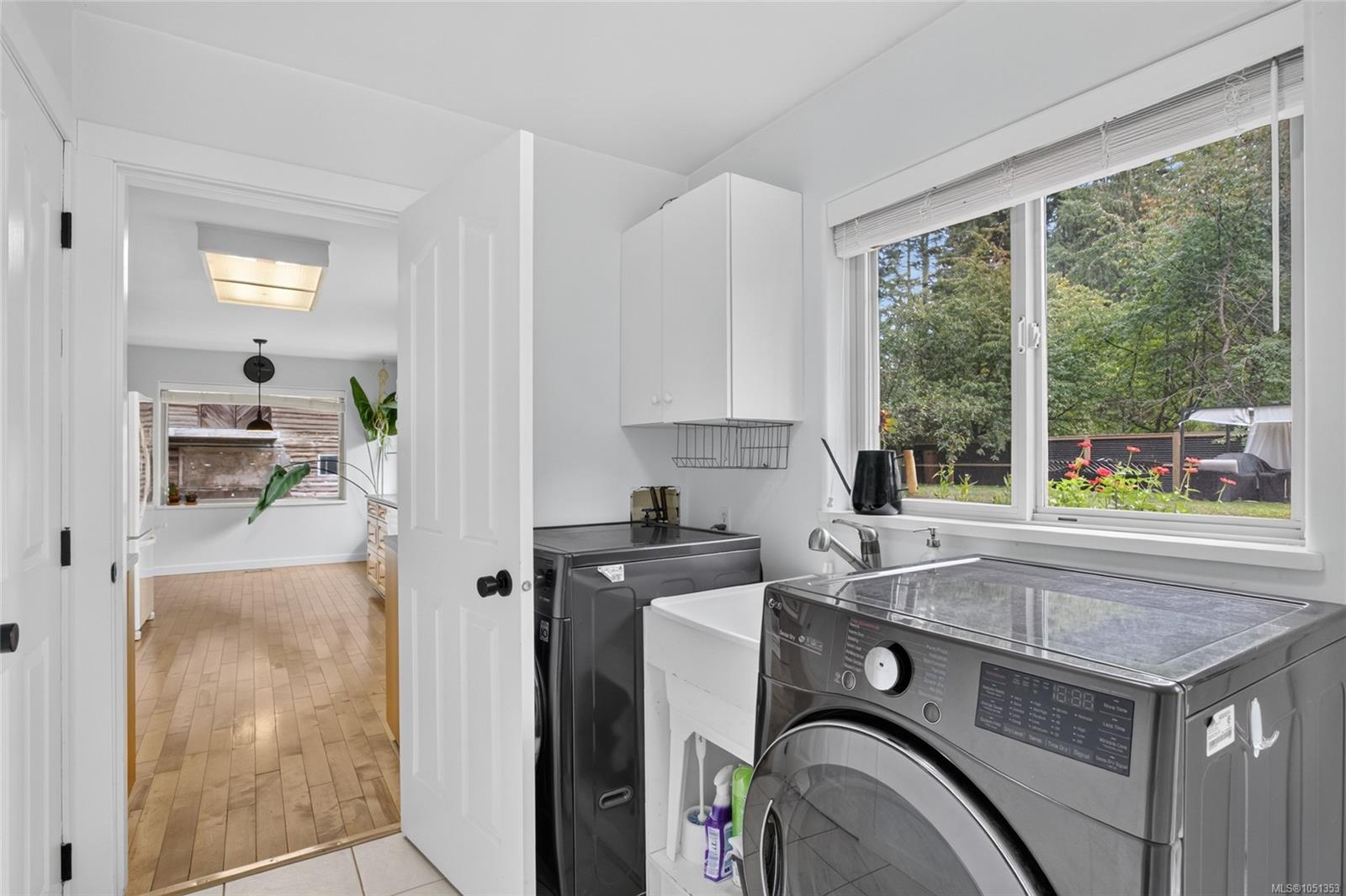 Laundry room with front-loading washer and dryer, utility sink, and a large backyard-facing window.